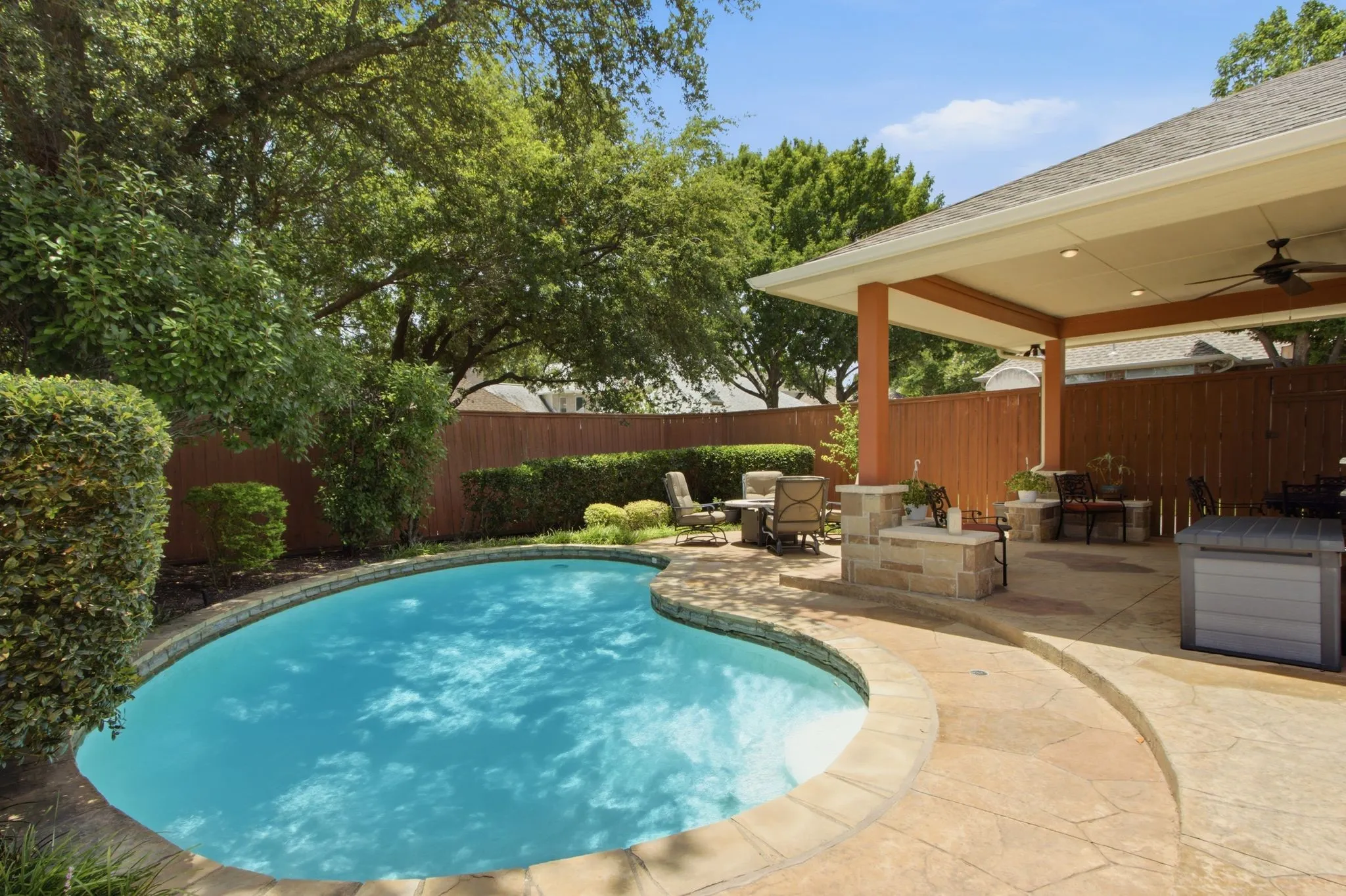 Curved swimming pool with stone coping, surrounded by stamped concrete patio