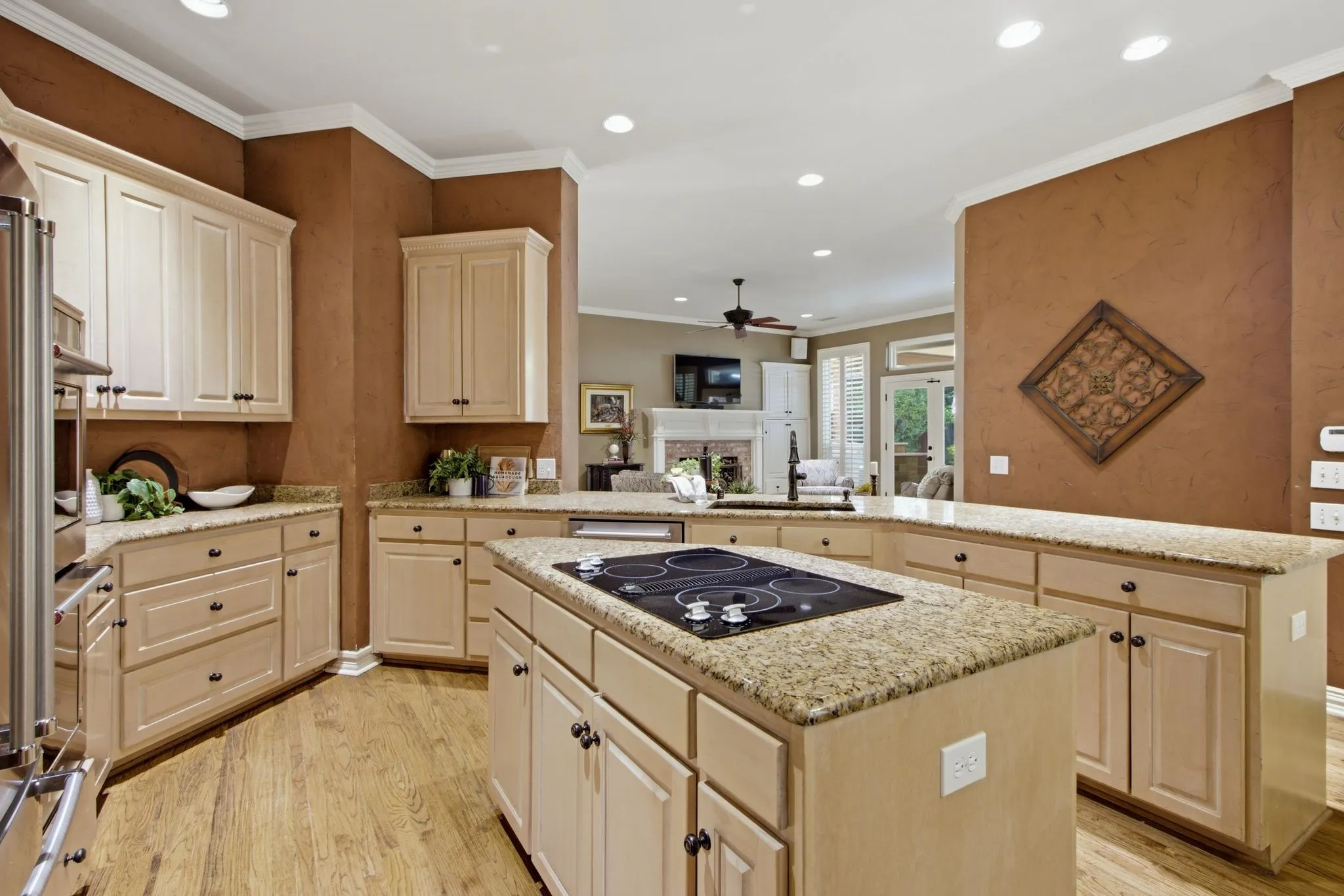 Kitchen featuring a central island with an integrated cooktop, light-toned cabinetry, and granite countertops