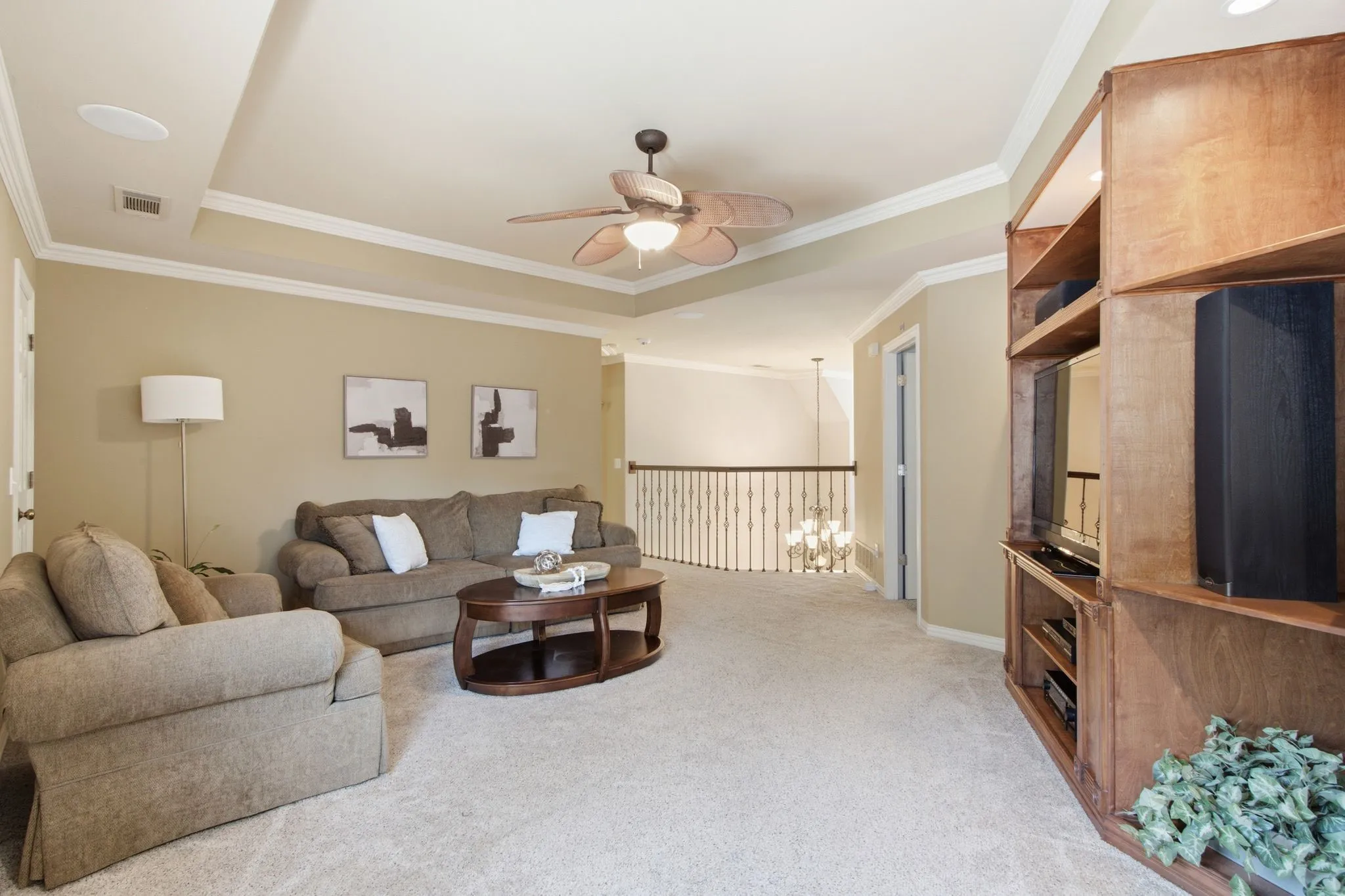 Carpeted living area featuring a built-in wood-finish media center, tray ceiling with a ceiling fan, and crown molding