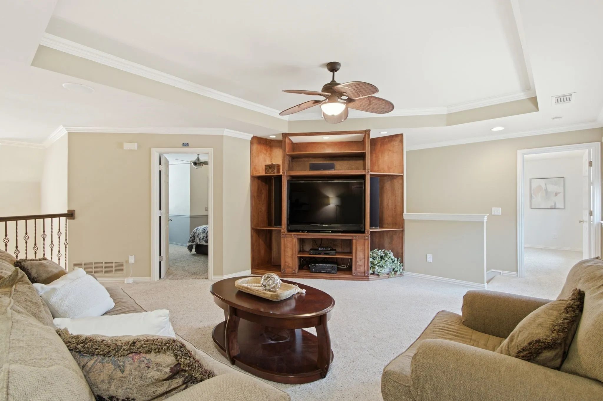 Carpeted upper-level living area featuring a built-in wood entertainment center with display shelving, a tray ceiling, and a ceiling fan