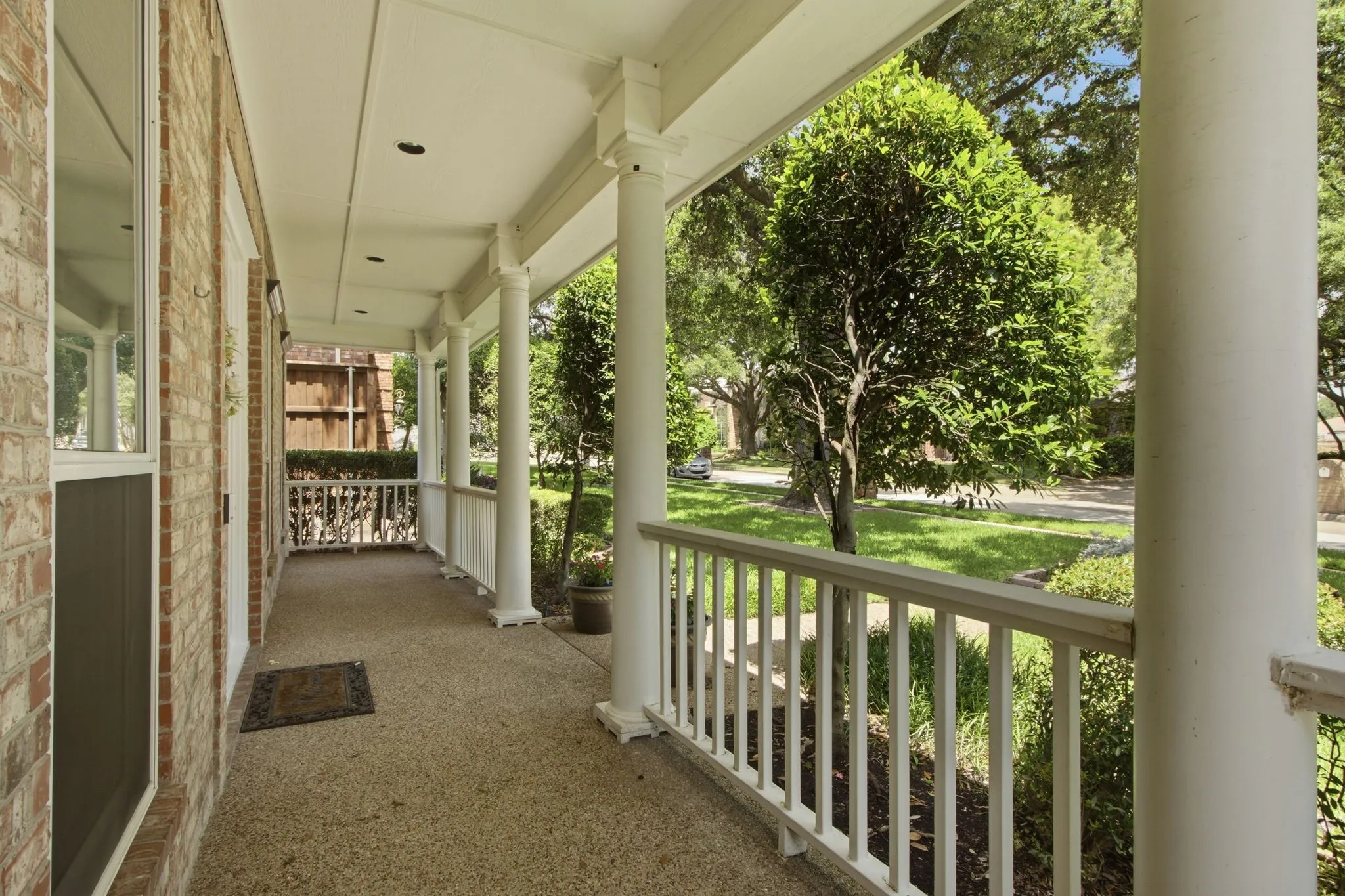 Inviting front porch featuring a brick exterior facade, white columns, a white railing, exposed aggregate flooring, and recessed ceiling lighting