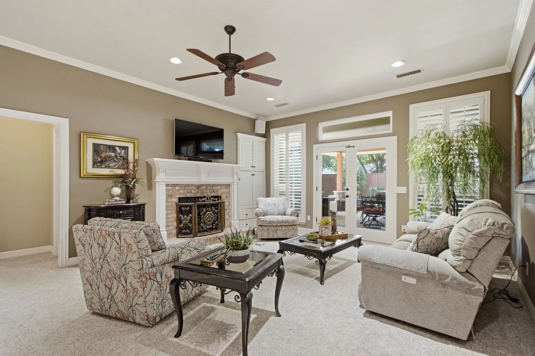 Living area featuring light-colored carpeting, a fireplace with a white mantel and brick surround, and built-in cabinetry