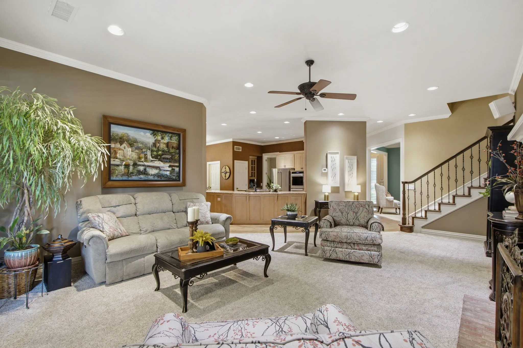 Carpeted living area featuring recessed lighting, a ceiling fan, crown molding, and a staircase with wrought iron balusters