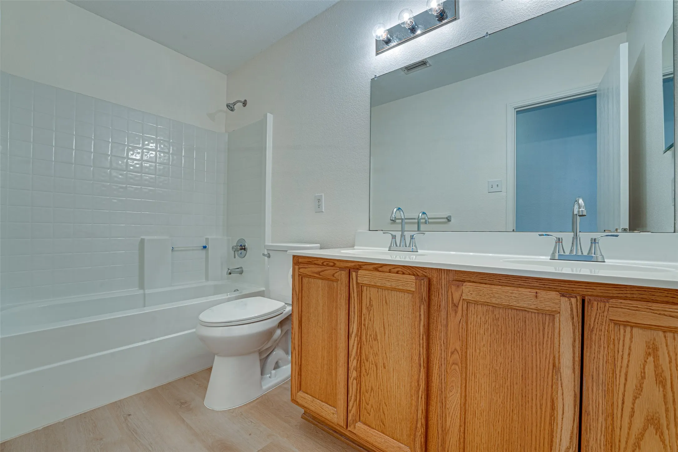 Bathroom featuring a double vanity with light wood cabinetry, white countertops, and dual chrome faucets