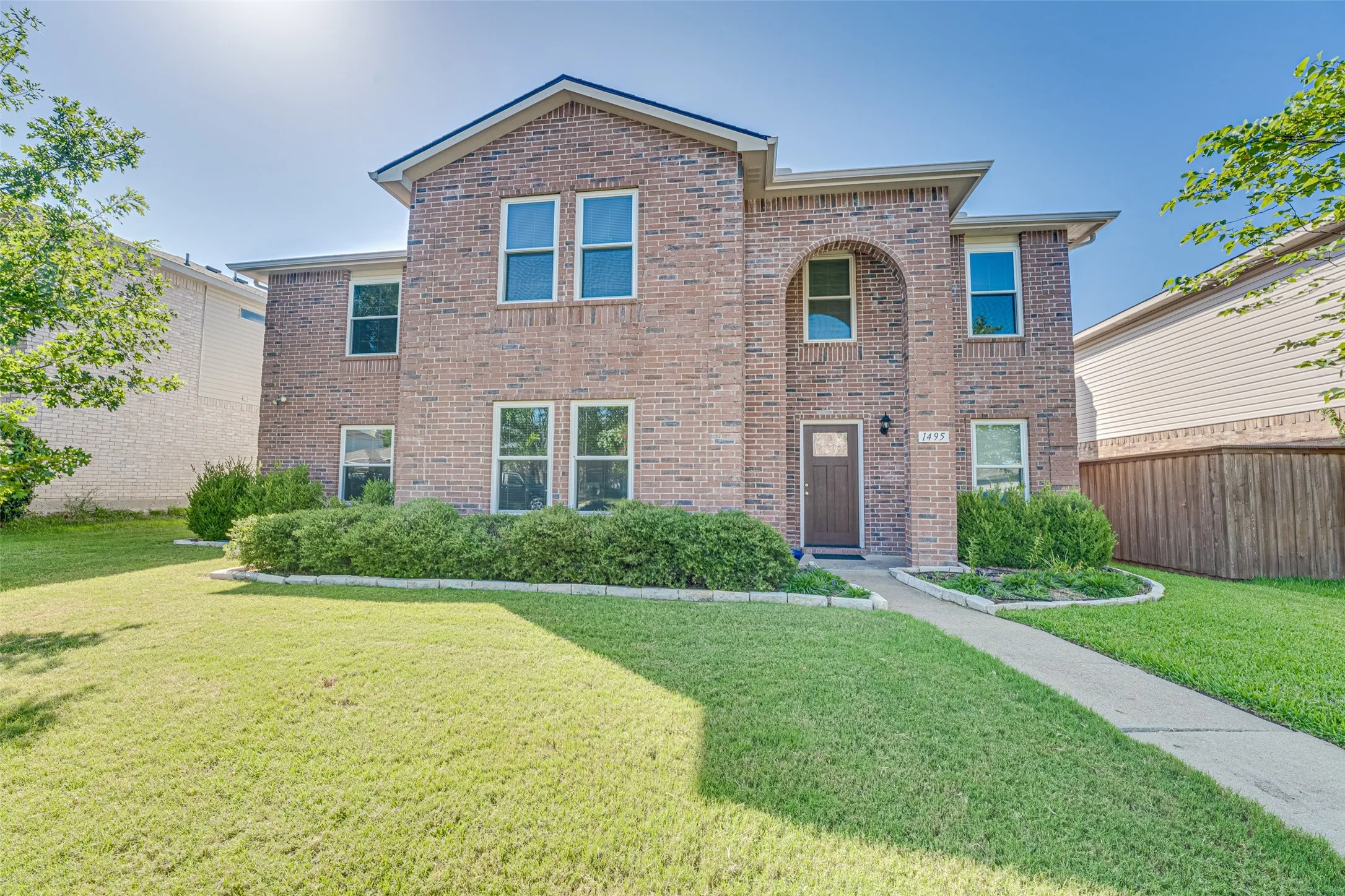 Brick facade residence featuring a two-story design, arched entry detail, and a concrete walkway