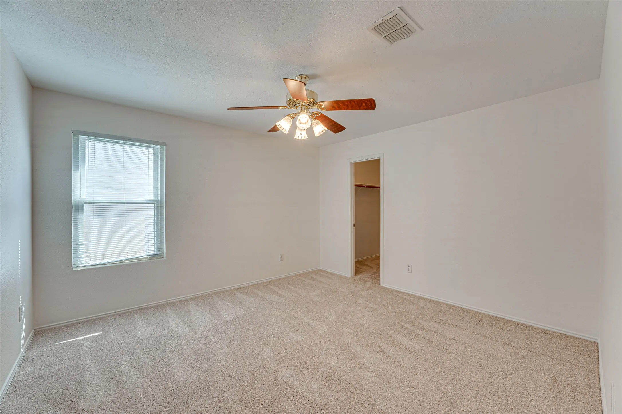 Neutral tone carpeted room with a ceiling fan light fixture, window with horizontal blinds, and a visible closet entry