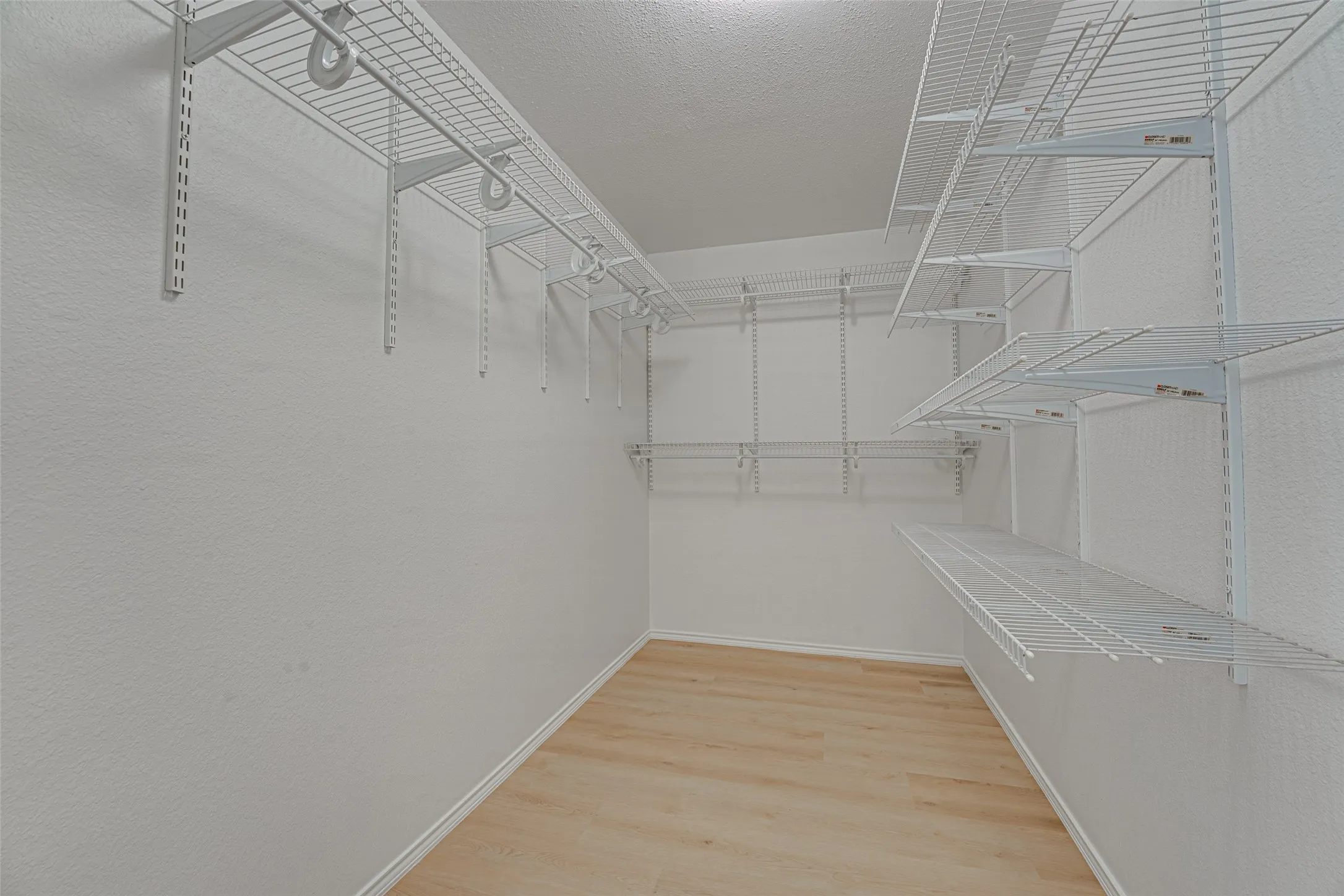 Walk-in closet featuring light wood-finish flooring, white painted walls, and extensive wire shelving and hanging systems