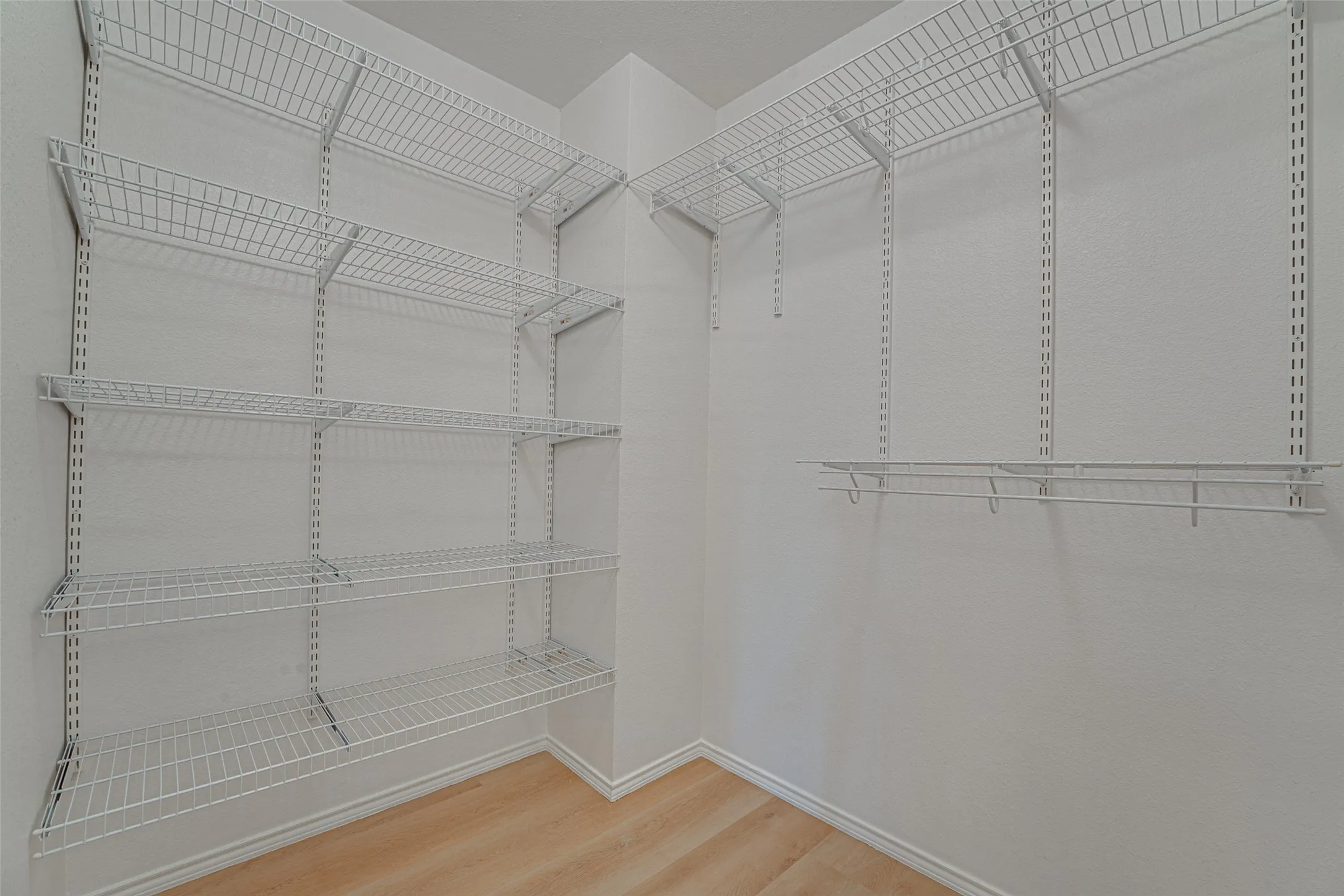 Walk-in closet featuring white wire shelving, white walls, and wood-finish flooring