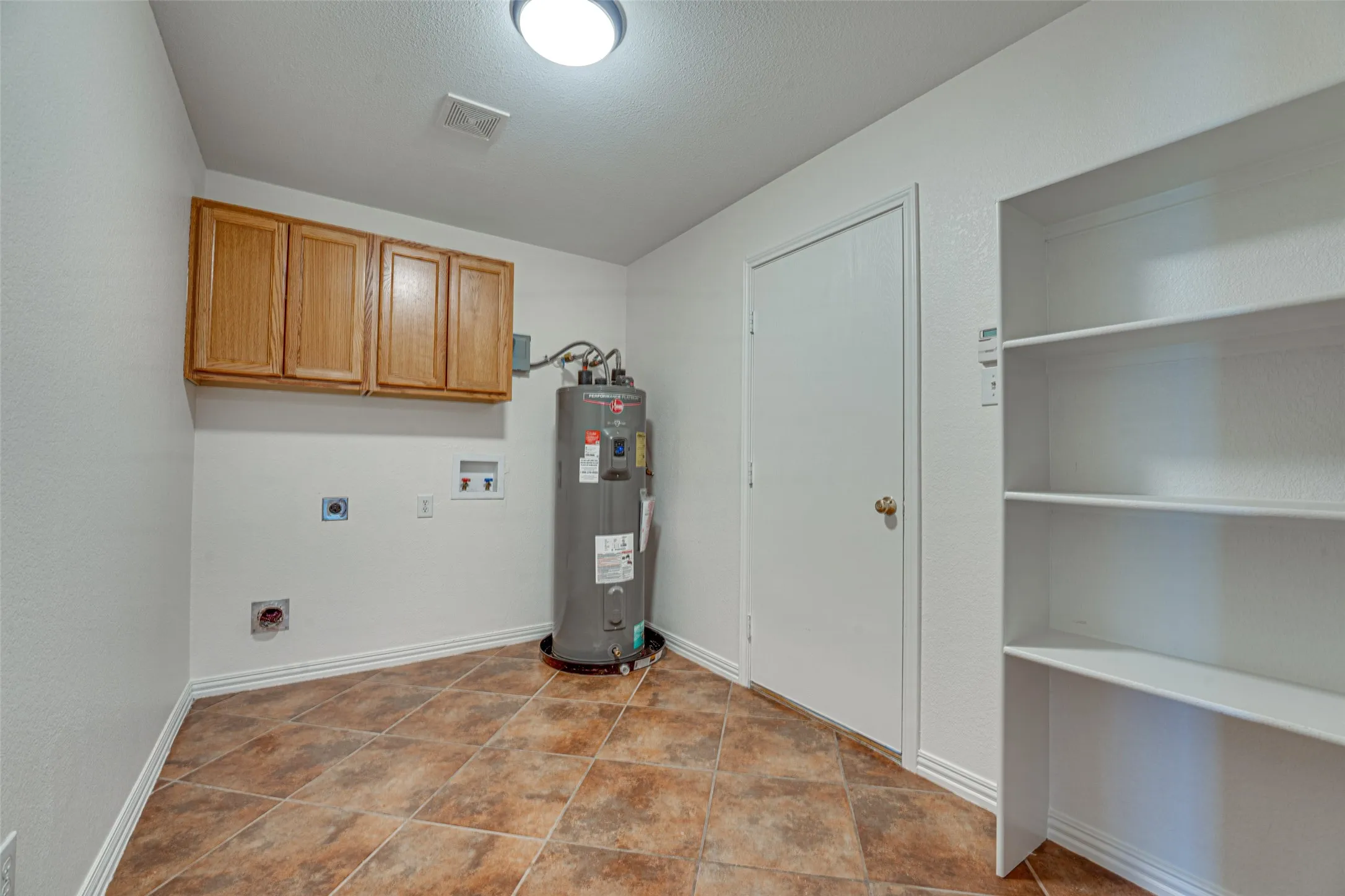 Utility room featuring tile flooring, built-in wooden cabinetry, white shelving, and a water heater