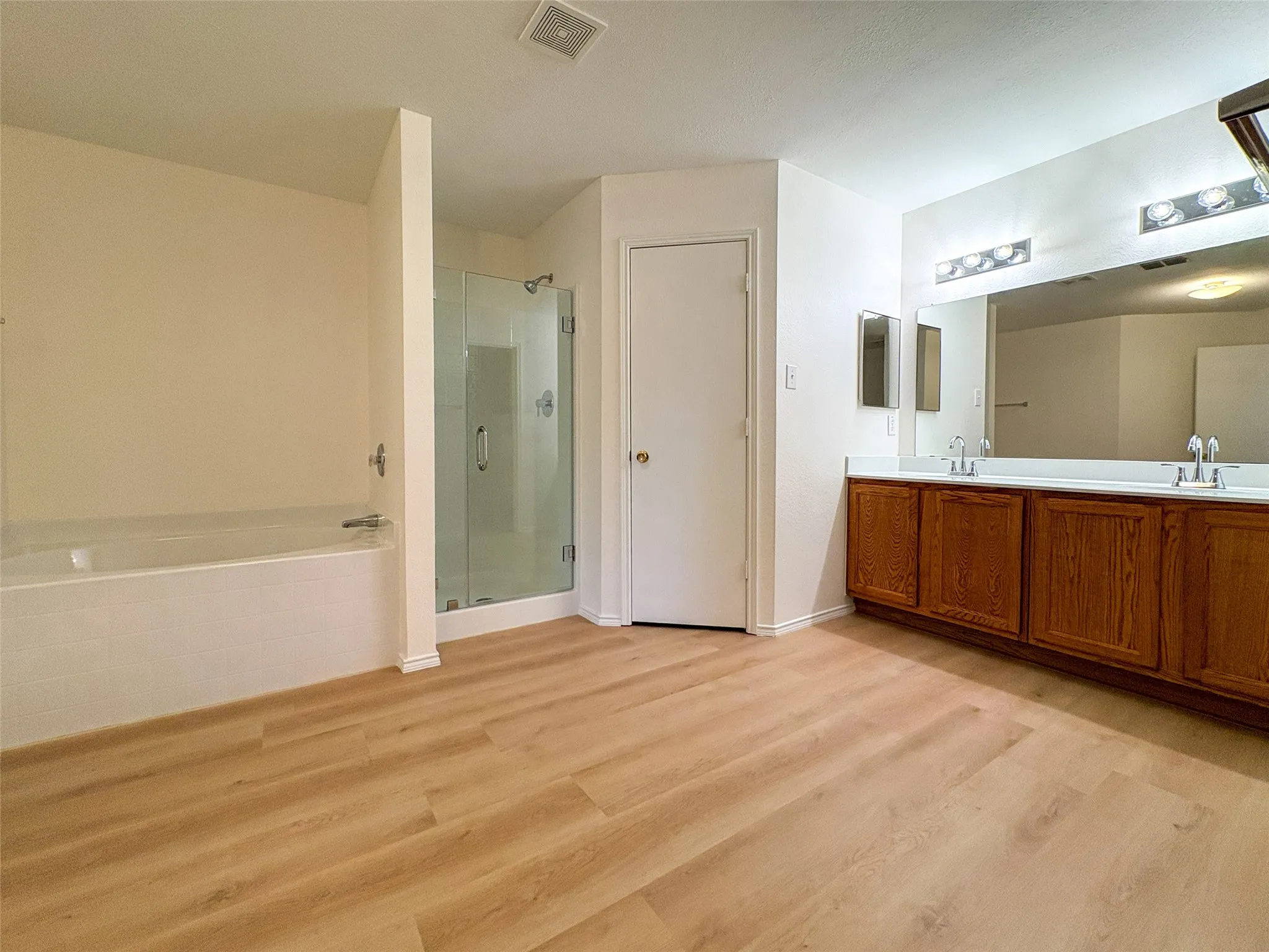 Bathroom featuring light wood-finish flooring, a white soaking tub, and a glass-enclosed shower