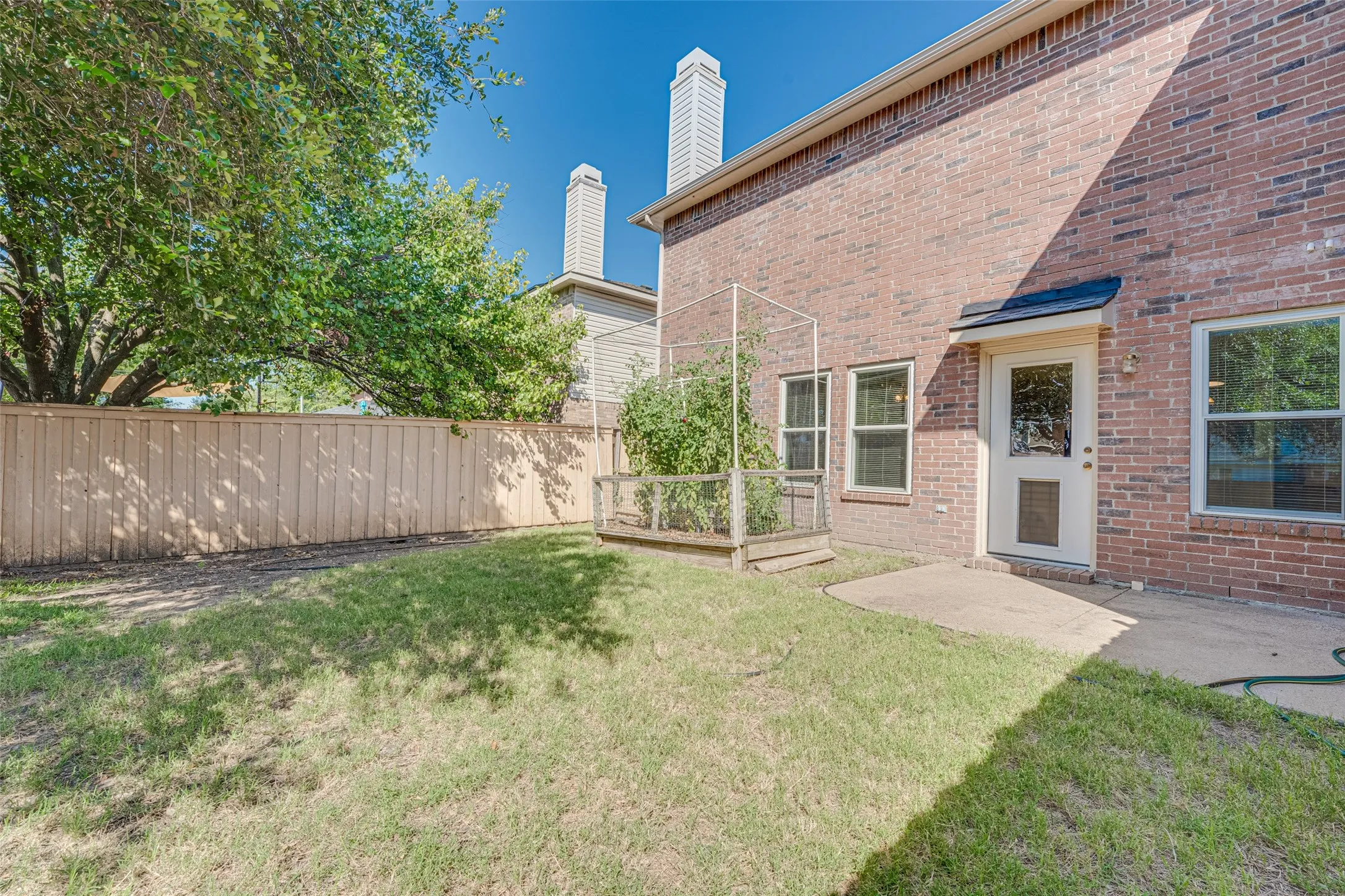 Expansive grassy backyard featuring a full privacy fence, mature trees, and a raised garden bed with a trellis