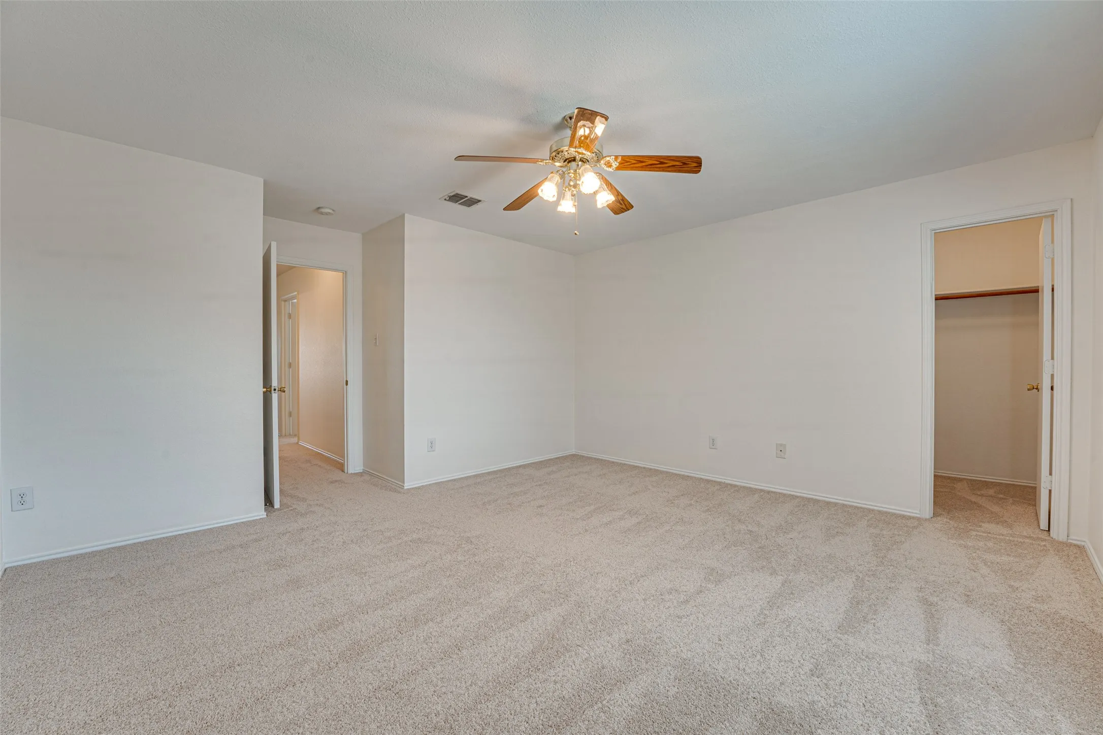 Carpeted room featuring a ceiling fan with integrated lighting, neutral wall tones, and multiple door openings