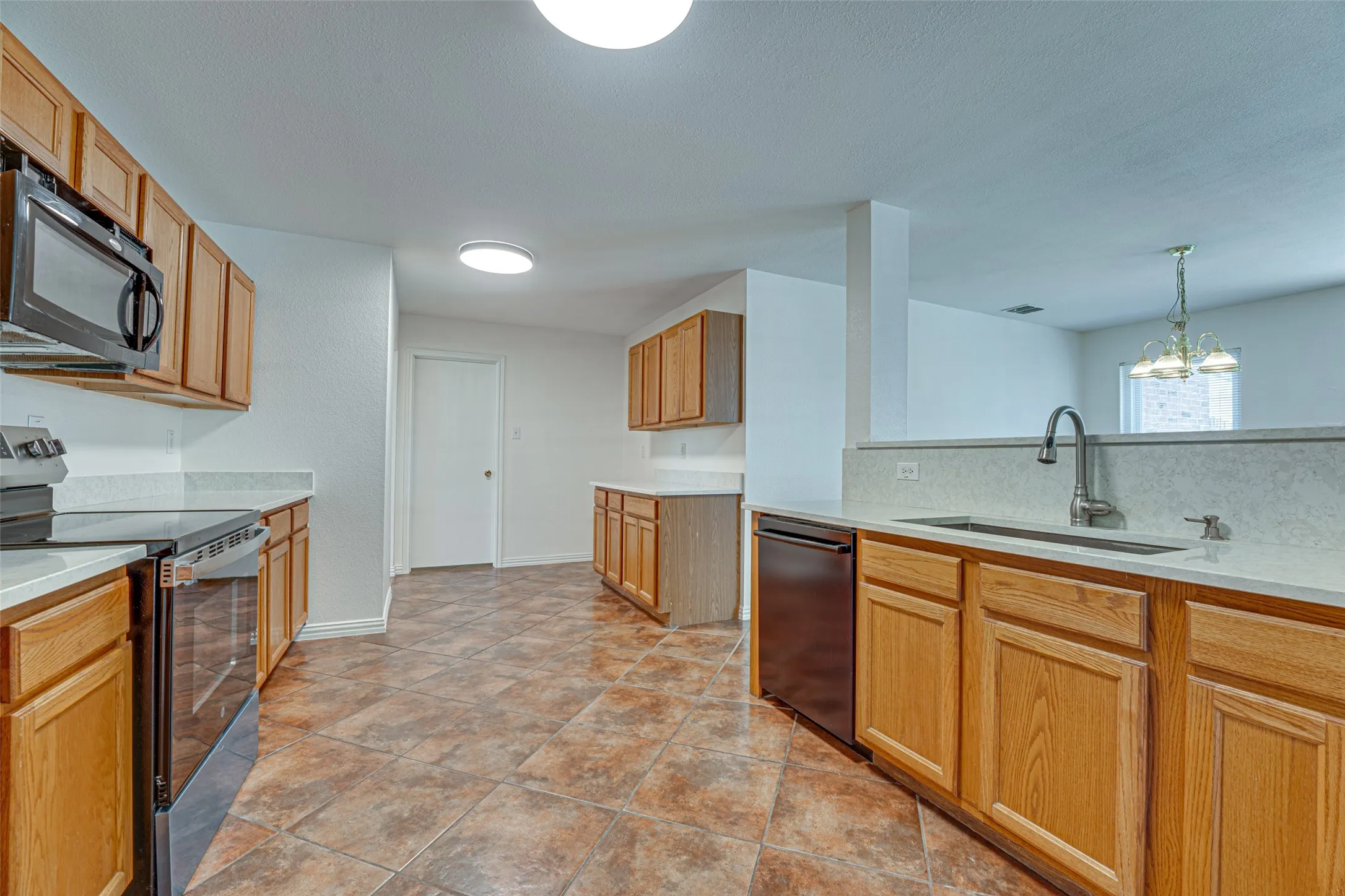 Kitchen featuring wood cabinetry, light-toned countertops, a stainless steel sink with a gooseneck faucet, black appliances, and tiled flooring