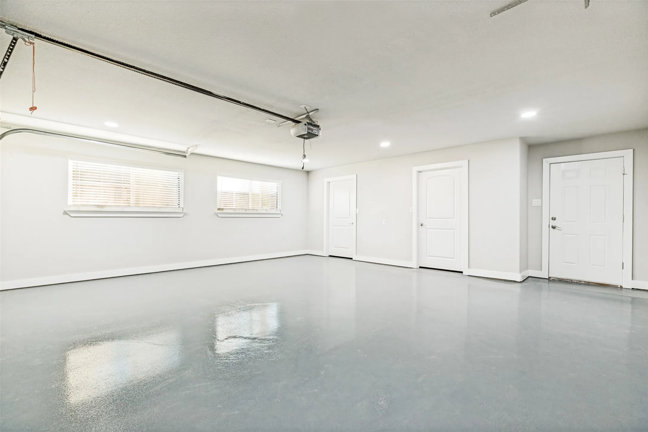 Spacious garage featuring a light gray epoxy floor finish, two windows with blinds, recessed lighting, and multiple paneled doors