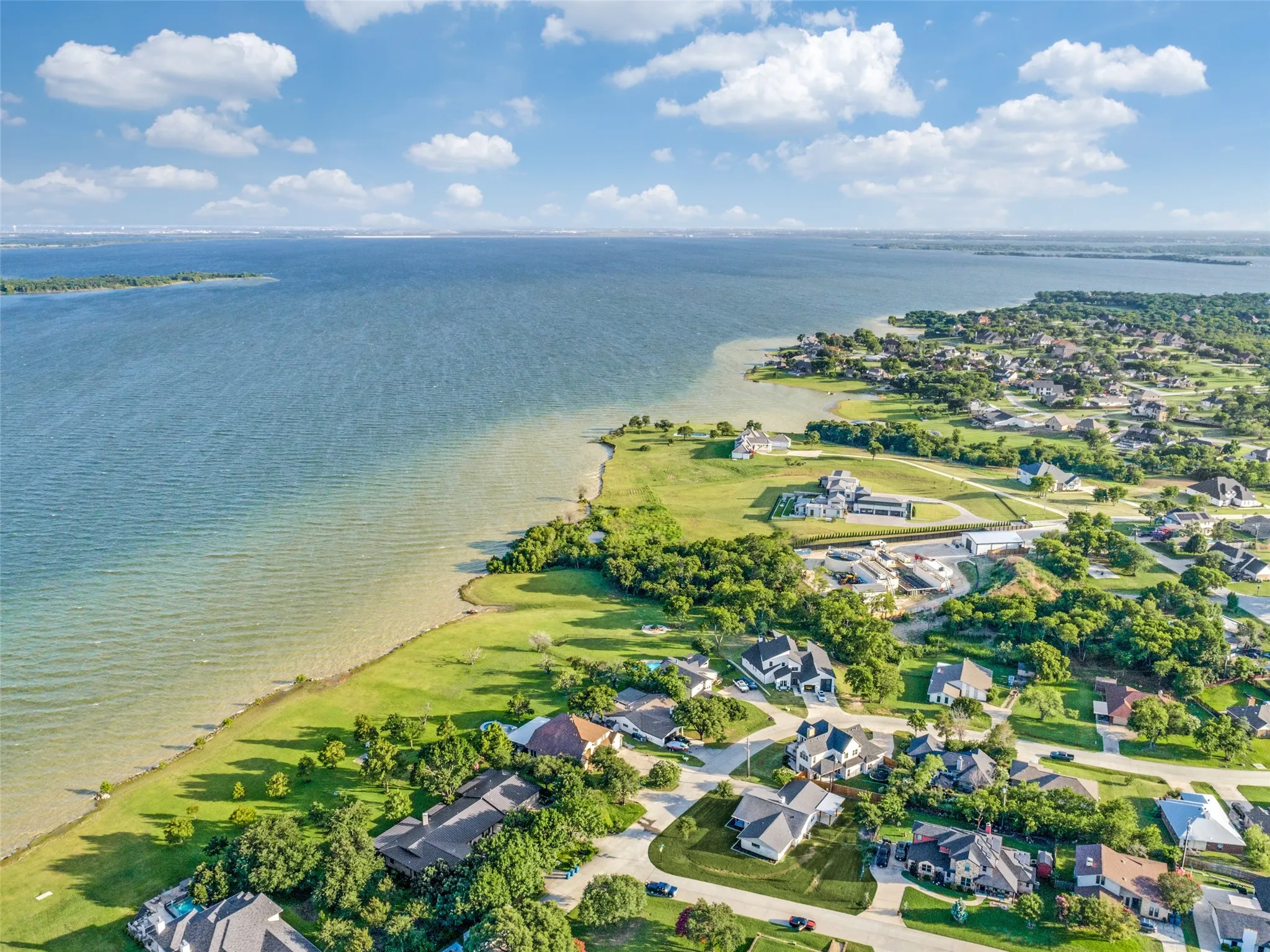 Expansive waterfront setting featuring a large body of water, lush green shoreline, and mature trees