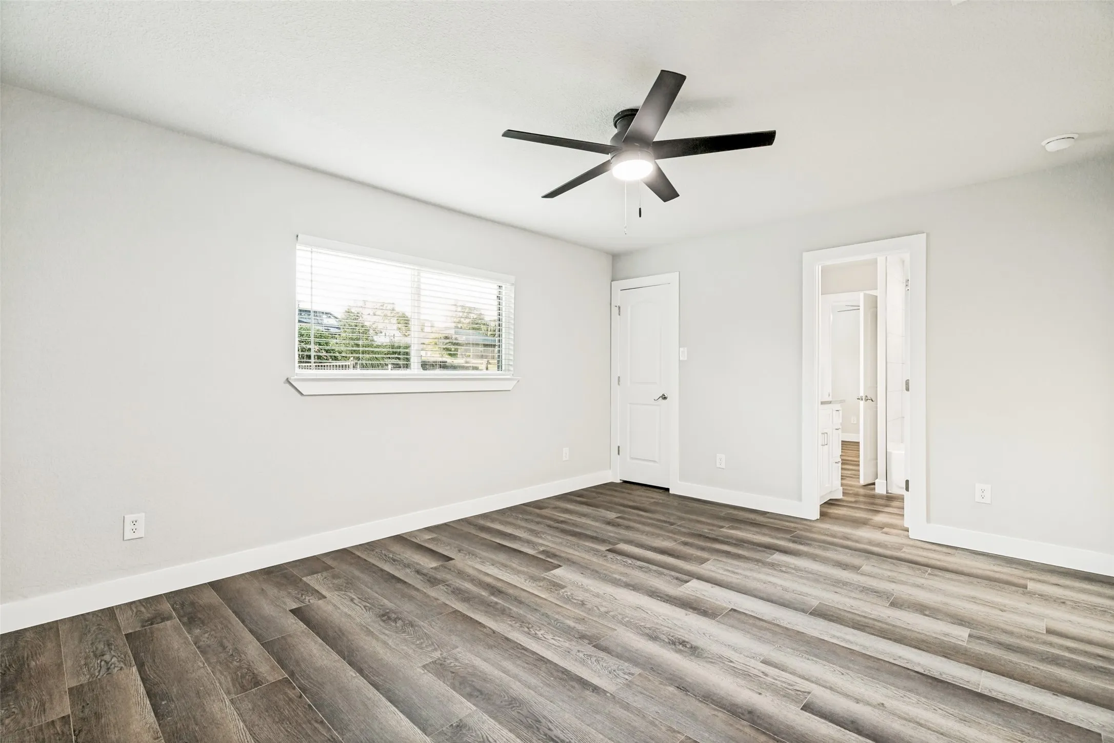 Spacious room featuring wood-finish flooring, light gray walls, white trim, and a contemporary ceiling fan