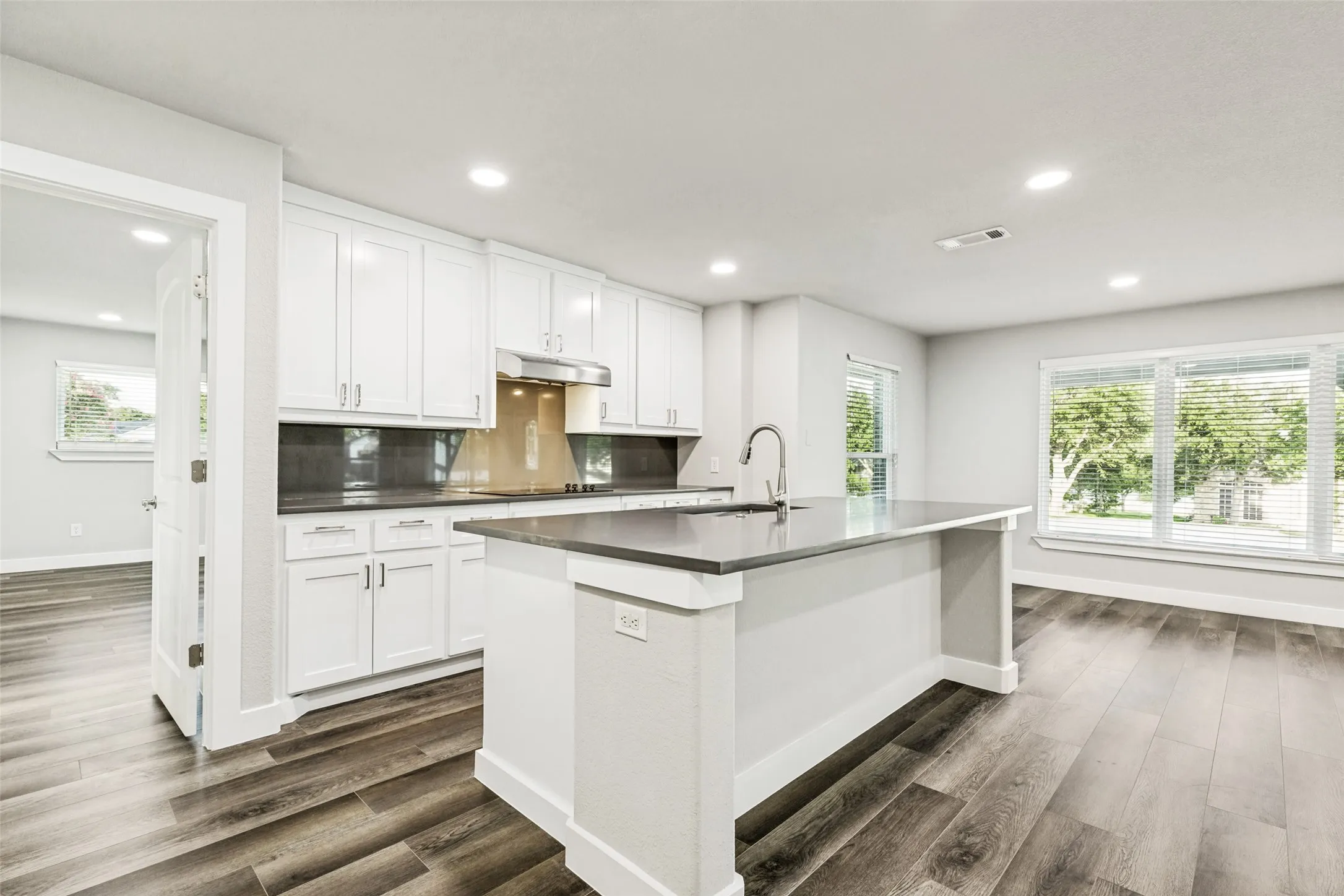 Contemporary kitchen featuring white cabinetry, dark countertops, and a central island with an integrated sink and faucet
