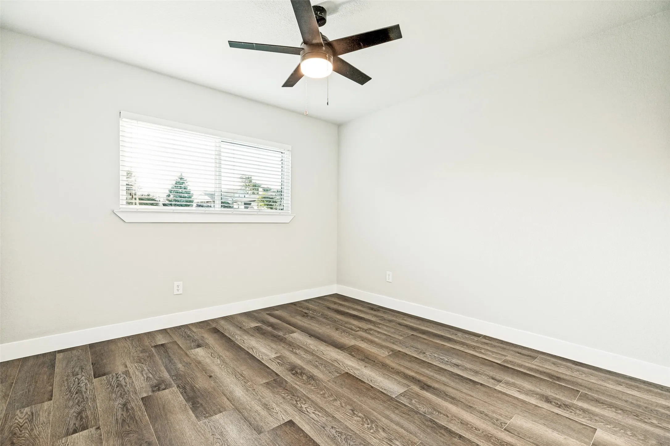 Room featuring wood-finish flooring, a window with horizontal blinds, and a ceiling fan with integrated lighting