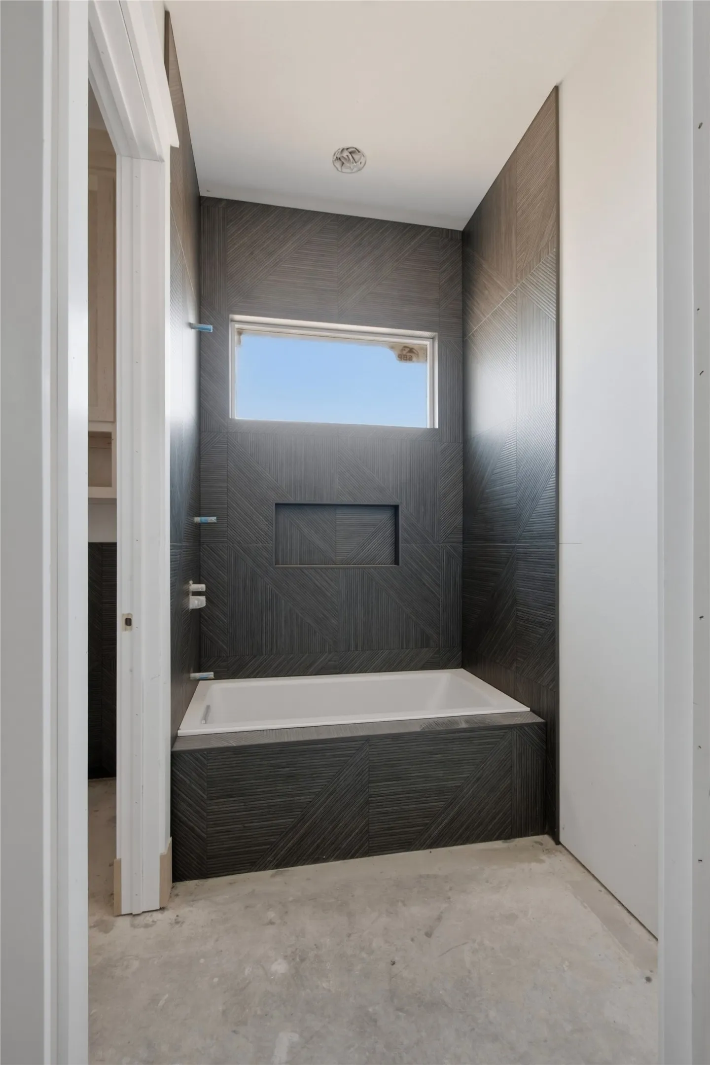 Bathroom featuring a built-in bathtub, textured dark tile surround, integrated shower niche, and an upper horizontal window