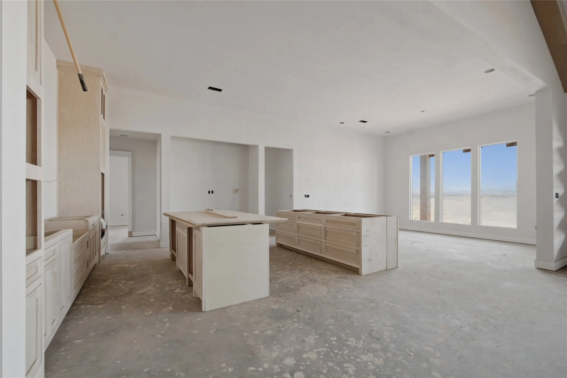 Spacious room featuring a smooth concrete floor, pre-installed cabinetry, and two kitchen islands awaiting finishes