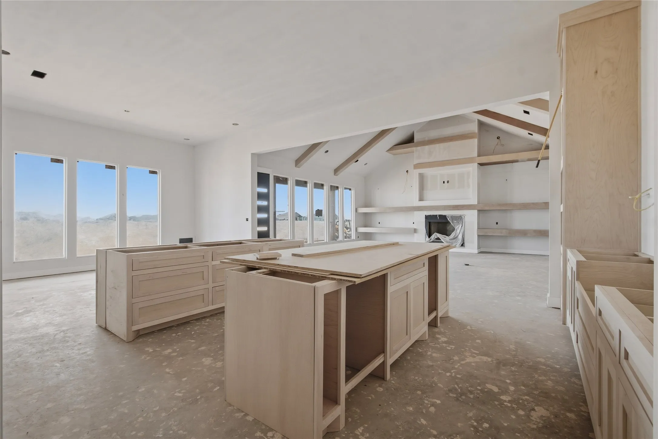 Spacious open-concept interior featuring light wood-finish cabinetry, a vaulted ceiling, and multiple large windows