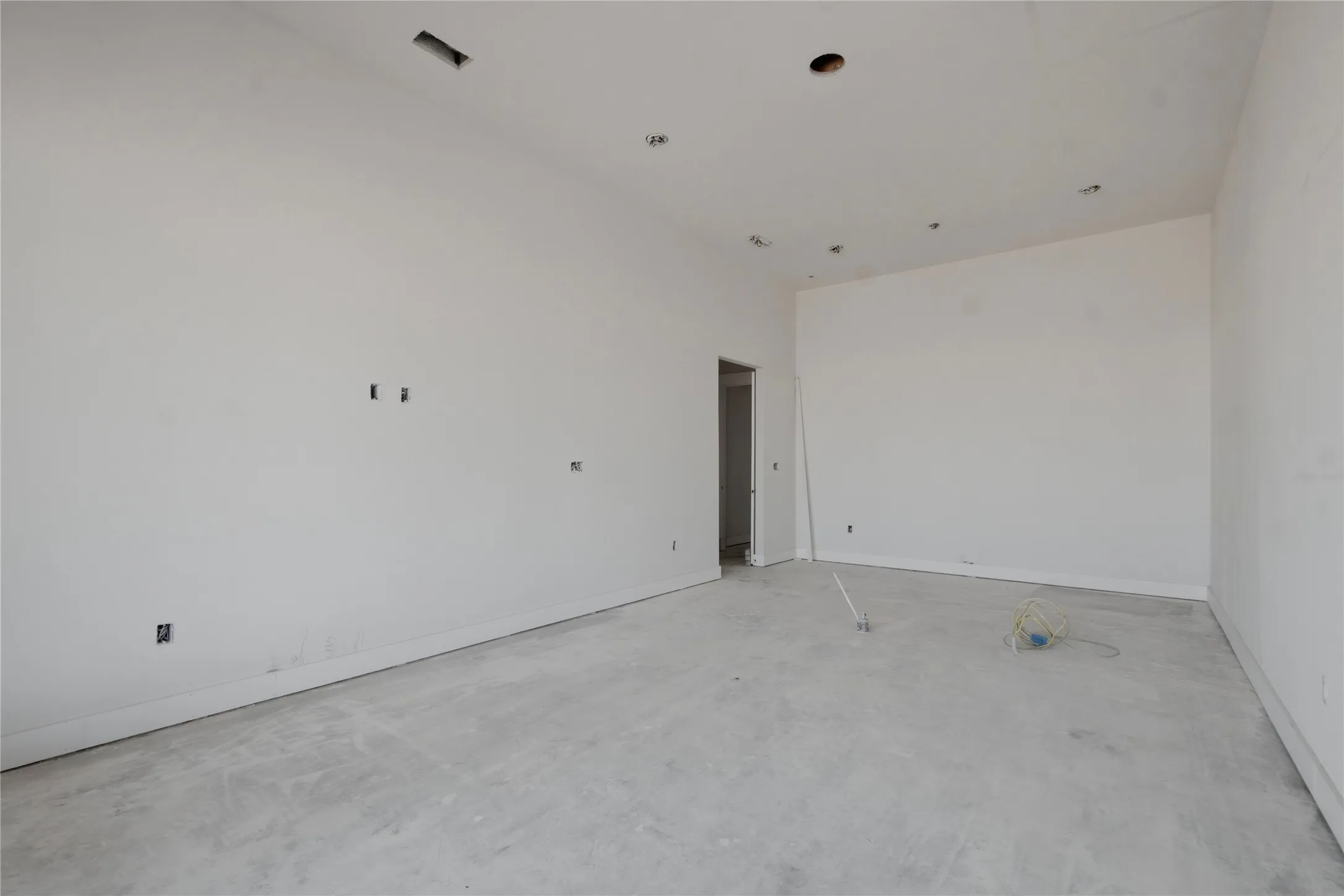 Spacious interior room with light-colored walls, concrete subflooring, recessed ceiling lighting, and multiple electrical outlets
