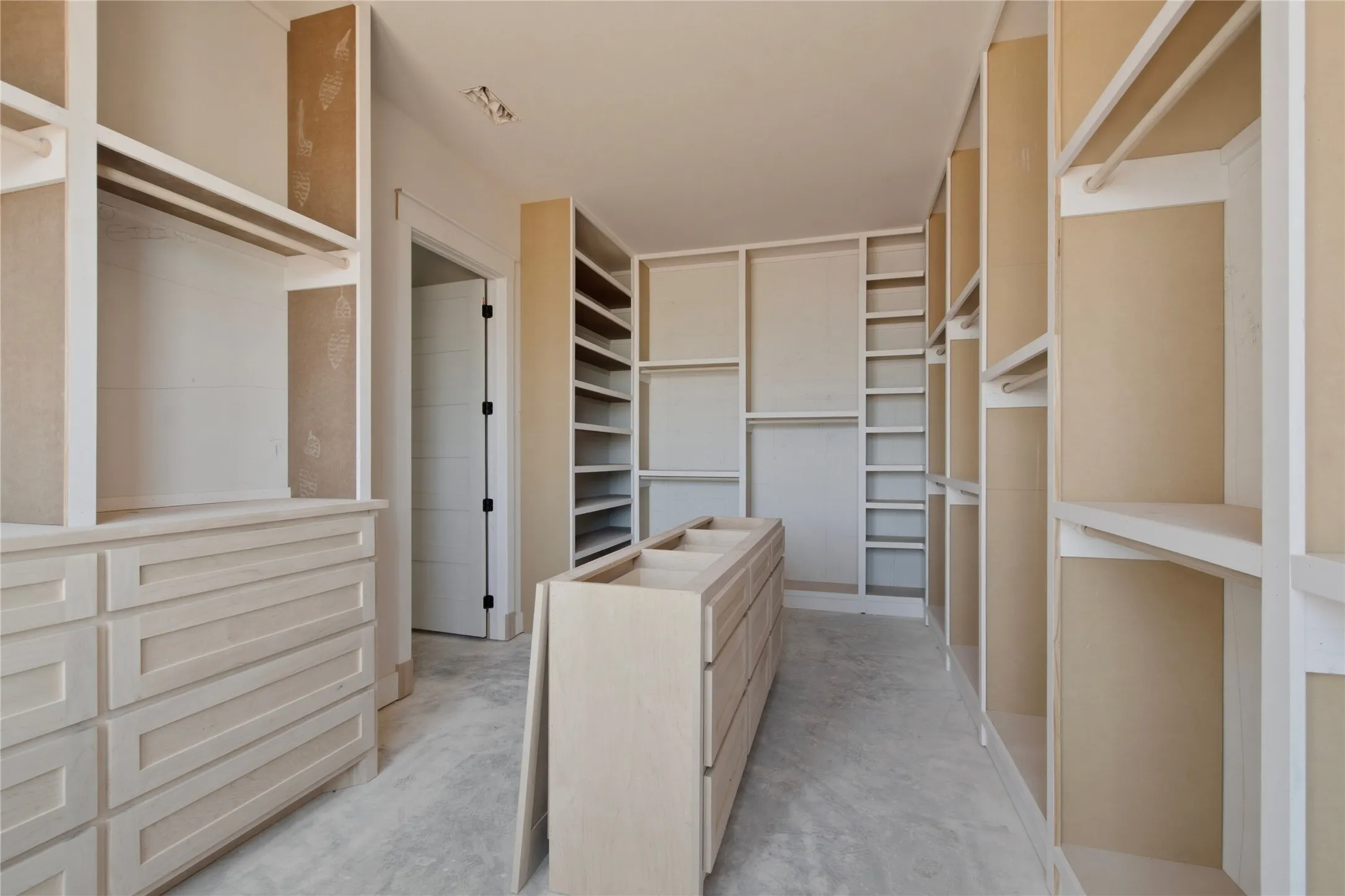 Walk-in closet featuring extensive built-in shelving, multiple hanging rods, a central island with integrated drawers, additional built-in drawer storage, and a light-colored wood-finish