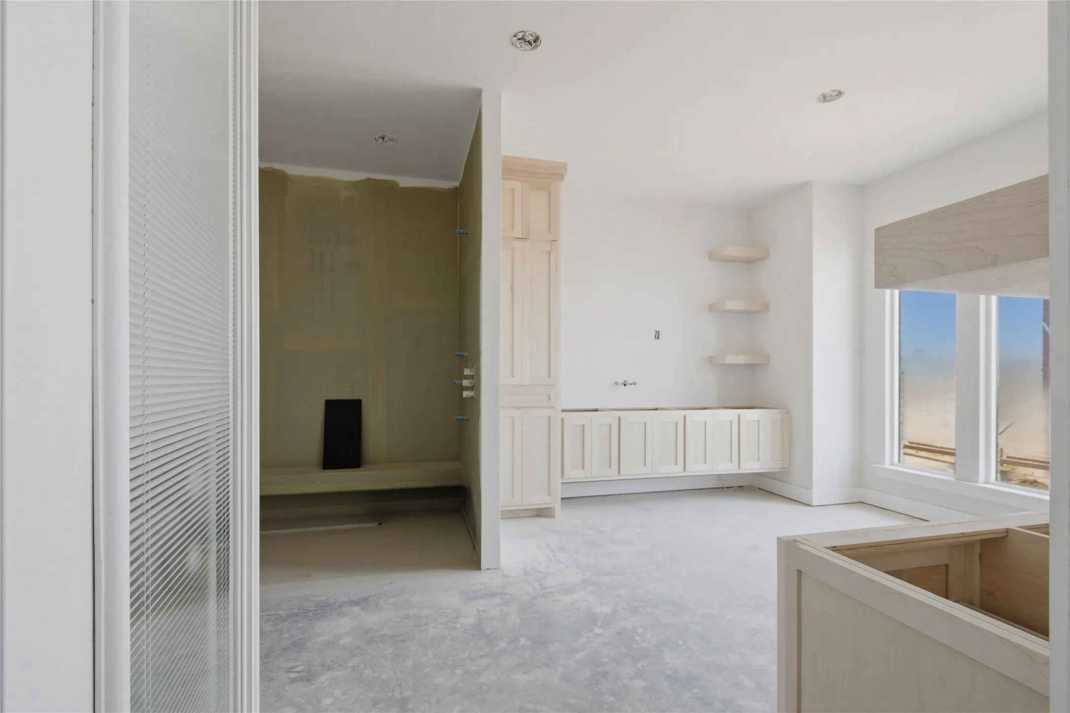 Unfinished interior space featuring a walk-in shower enclosure with a built-in bench, light-toned cabinetry, corner shelving, and windows providing natural light