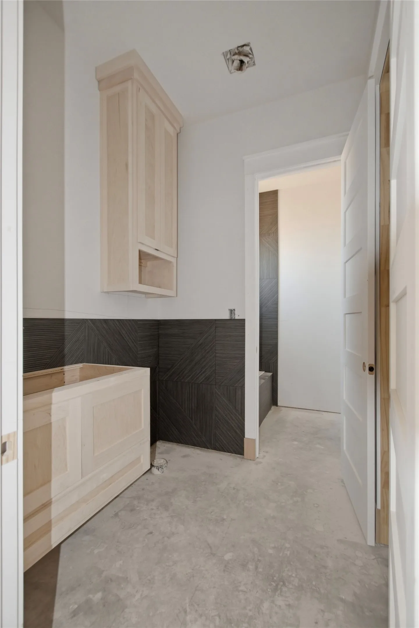 Bathroom vanity area featuring light wood-finish cabinetry, a built-in base, and dark geometric-patterned wall tiling