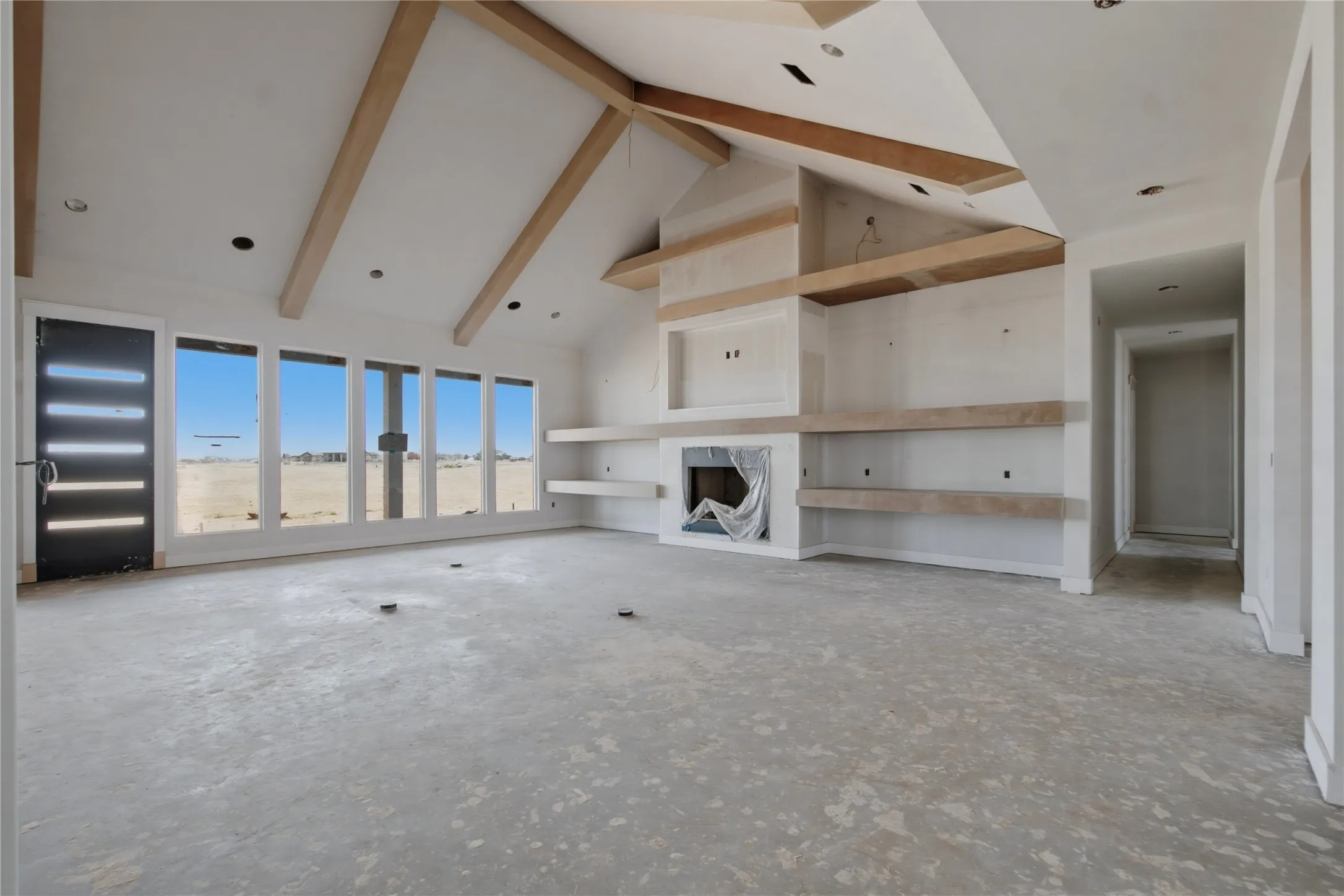 Spacious living area featuring a vaulted ceiling with exposed wood beams, a contemporary fireplace, and built-in shelving
