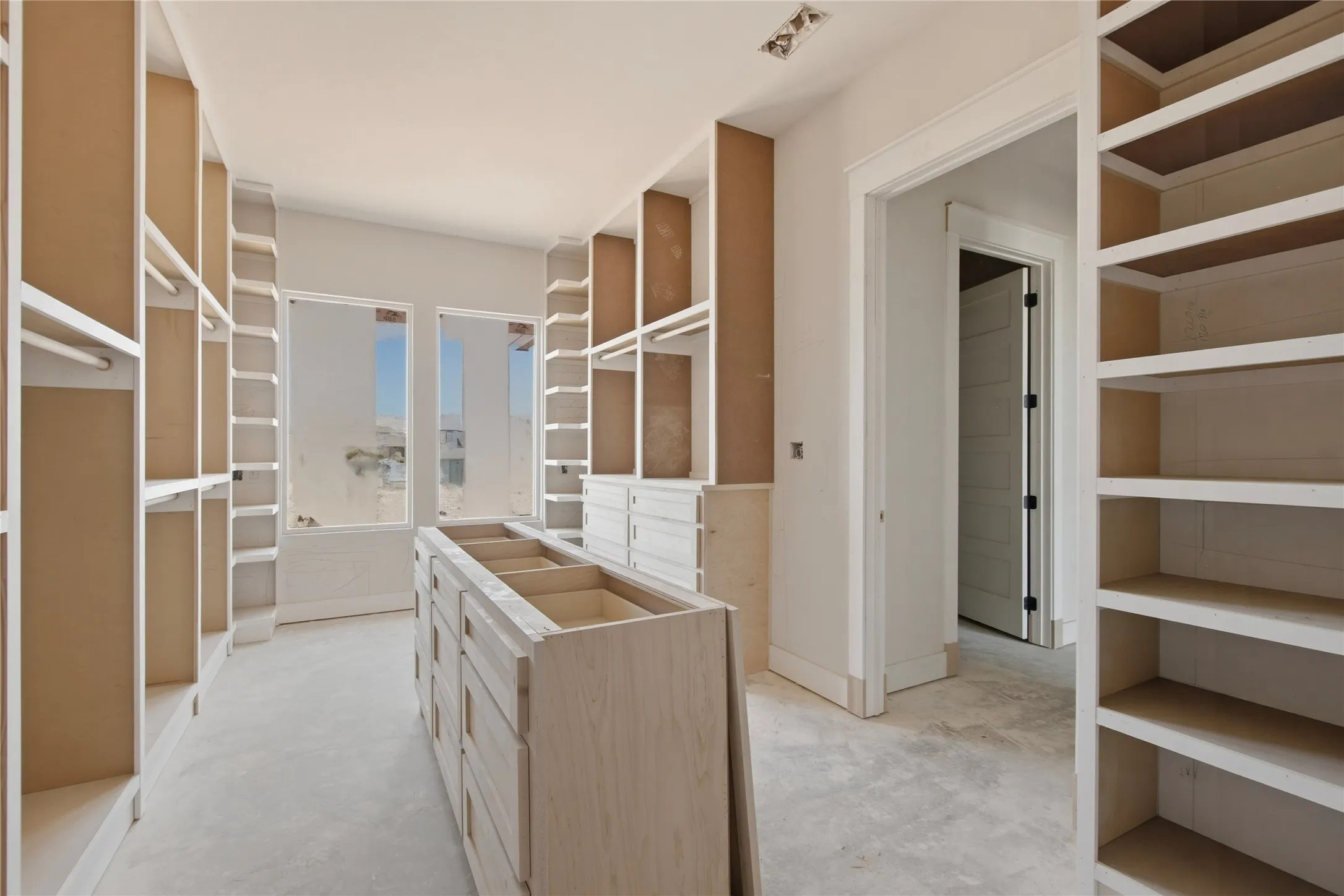 Spacious dressing room featuring extensive built-in shelving, multiple hanging rods, a central island with integrated drawers, and ample natural light from two windows