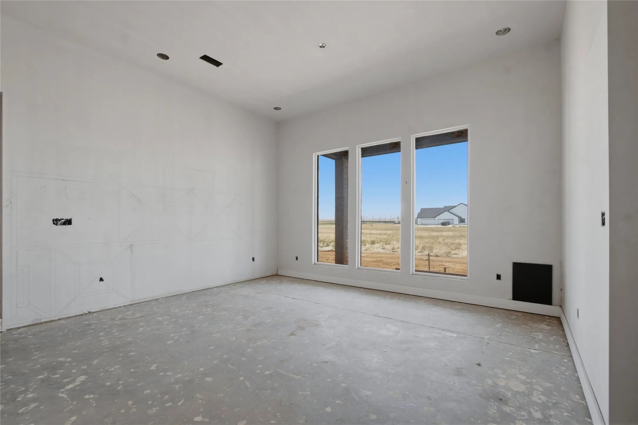 Spacious interior featuring a concrete subfloor, multiple large windows, recessed ceiling lighting, and a neutral wall finish