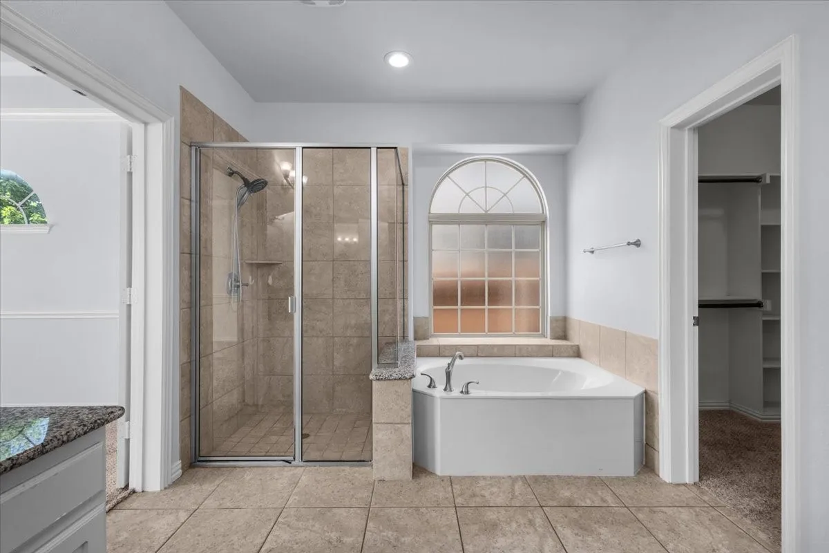 Spacious bathroom featuring a corner soaking tub, tiled shower enclosure with glass doors, and arched window