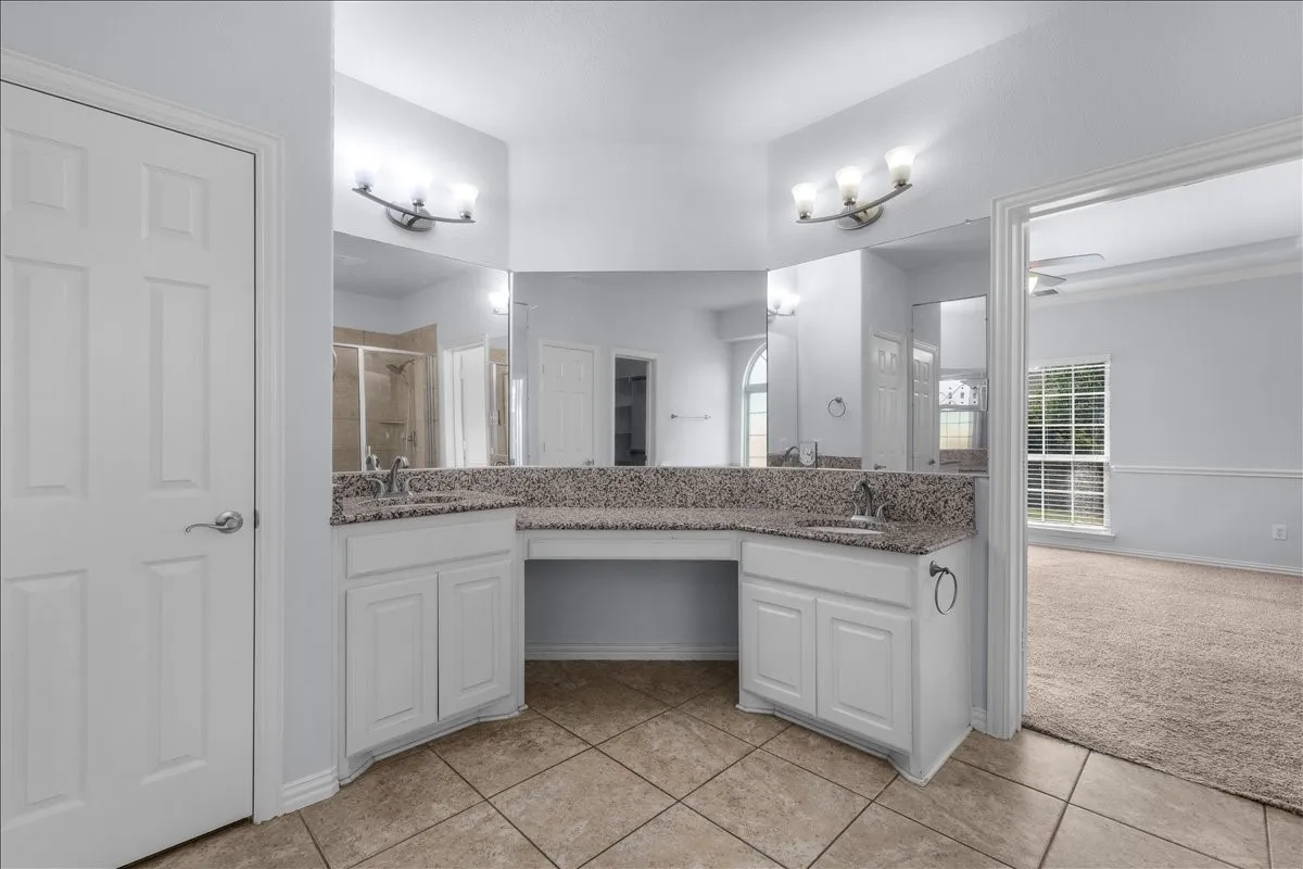 Double vanity with granite countertops, integrated sinks, white cabinetry, and a dedicated vanity area