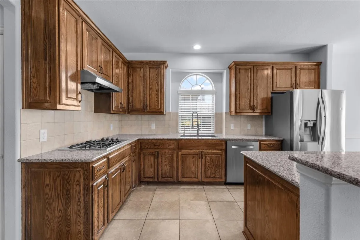 Kitchen featuring wood cabinetry, granite countertops, tile flooring, and stainless steel appliances including a gas range and refrigerator