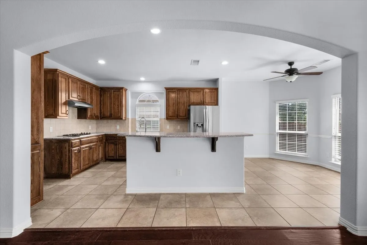 Open-concept kitchen and dining area featuring warm wood cabinetry, a central island with countertop seating, stainless steel appliances, and tiled flooring