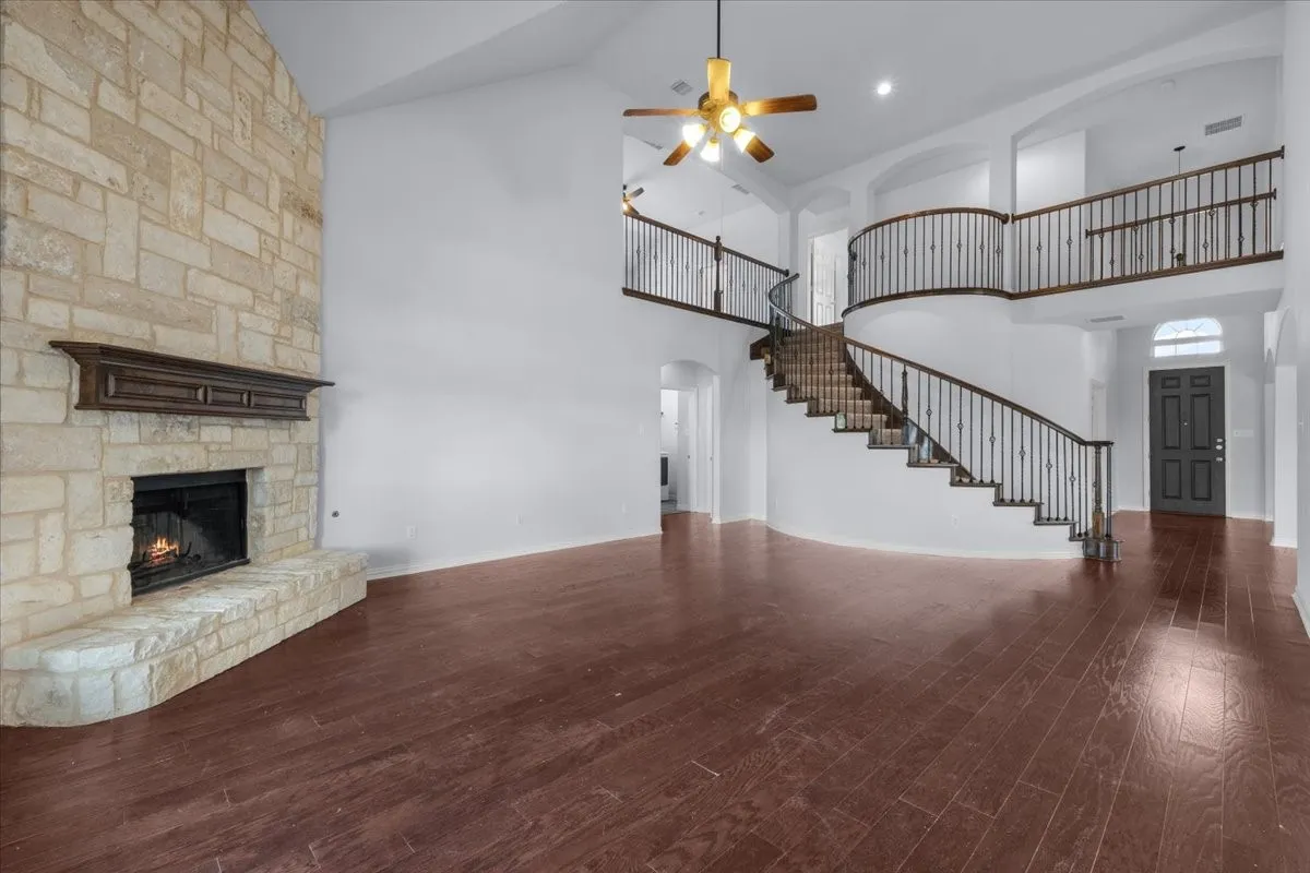Spacious living area featuring a floor-to-ceiling stone fireplace, dark wood-finish flooring, and a grand curved staircase with wrought iron balusters