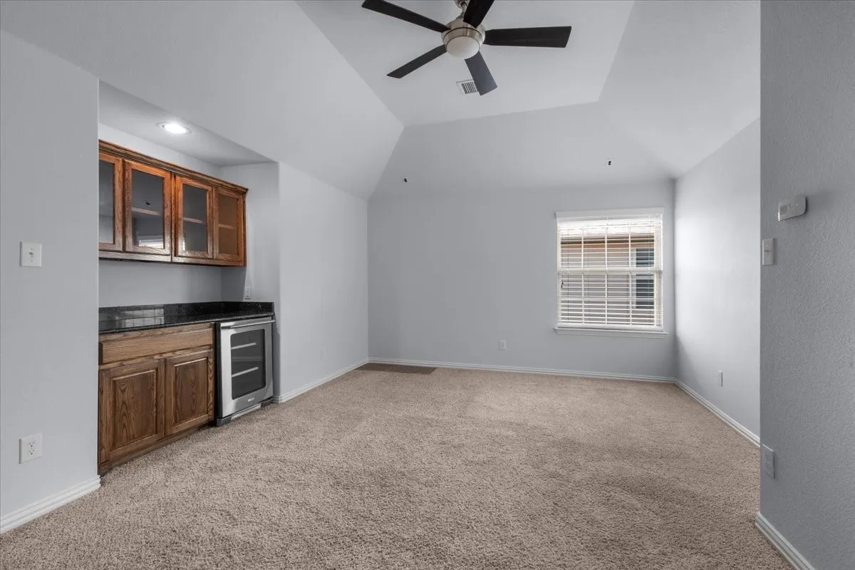 Spacious carpeted room featuring a built-in wet bar with wood cabinetry, dark countertop, and an under-counter beverage cooler