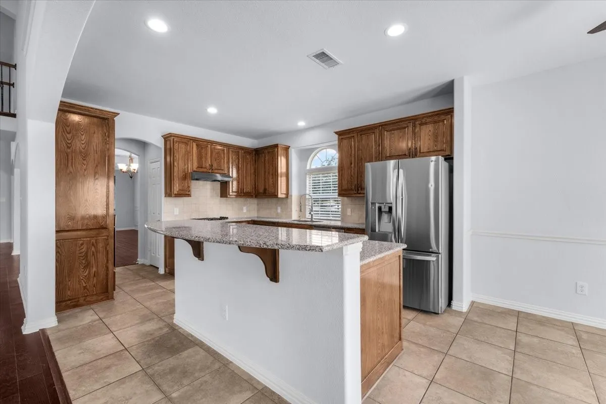Kitchen featuring wood cabinetry, granite countertops, tile flooring, and stainless steel appliances