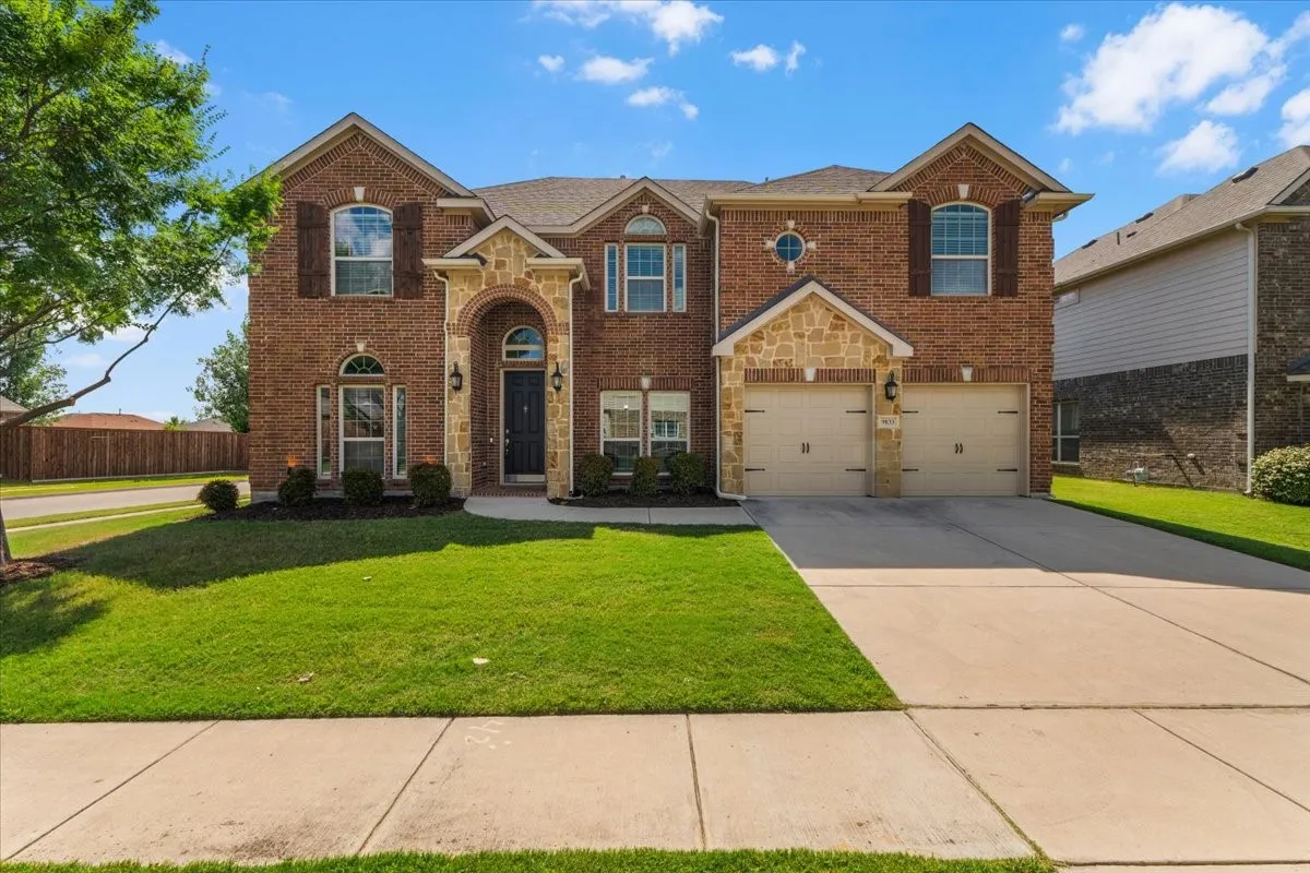 Two-story brick exterior featuring stone accents, a dual-door garage, an arched entry, and shuttered windows