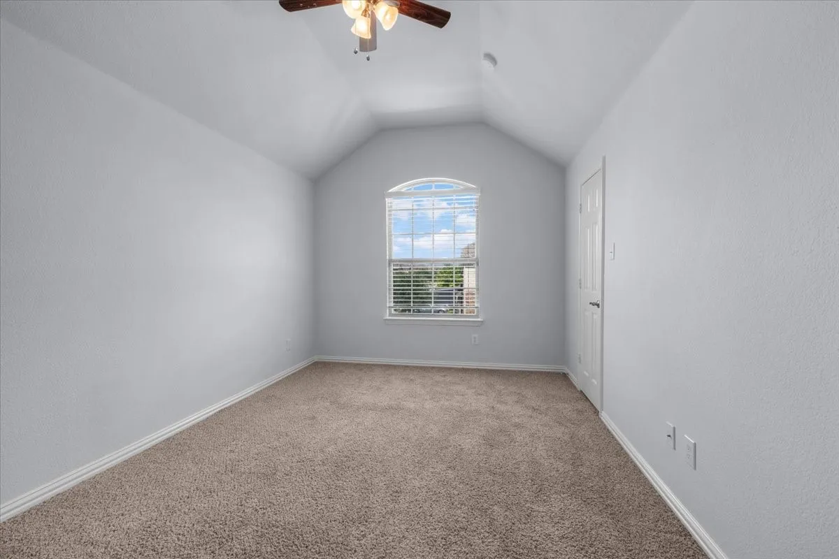 Vaulted ceiling room with an arched window featuring blinds, textured walls, light-colored carpet, and a ceiling fan with light fixture