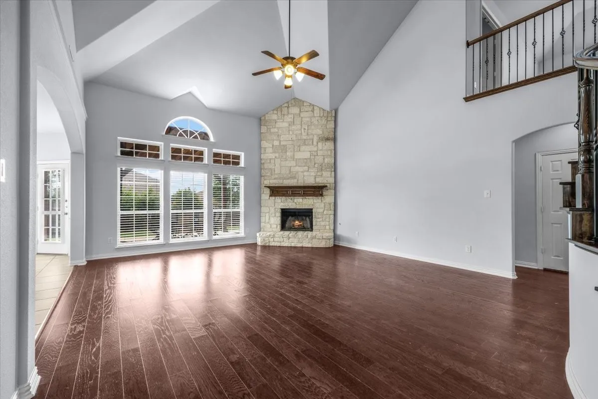 Spacious living area featuring high vaulted ceilings, large picture windows with a stone-faced fireplace with wood mantel