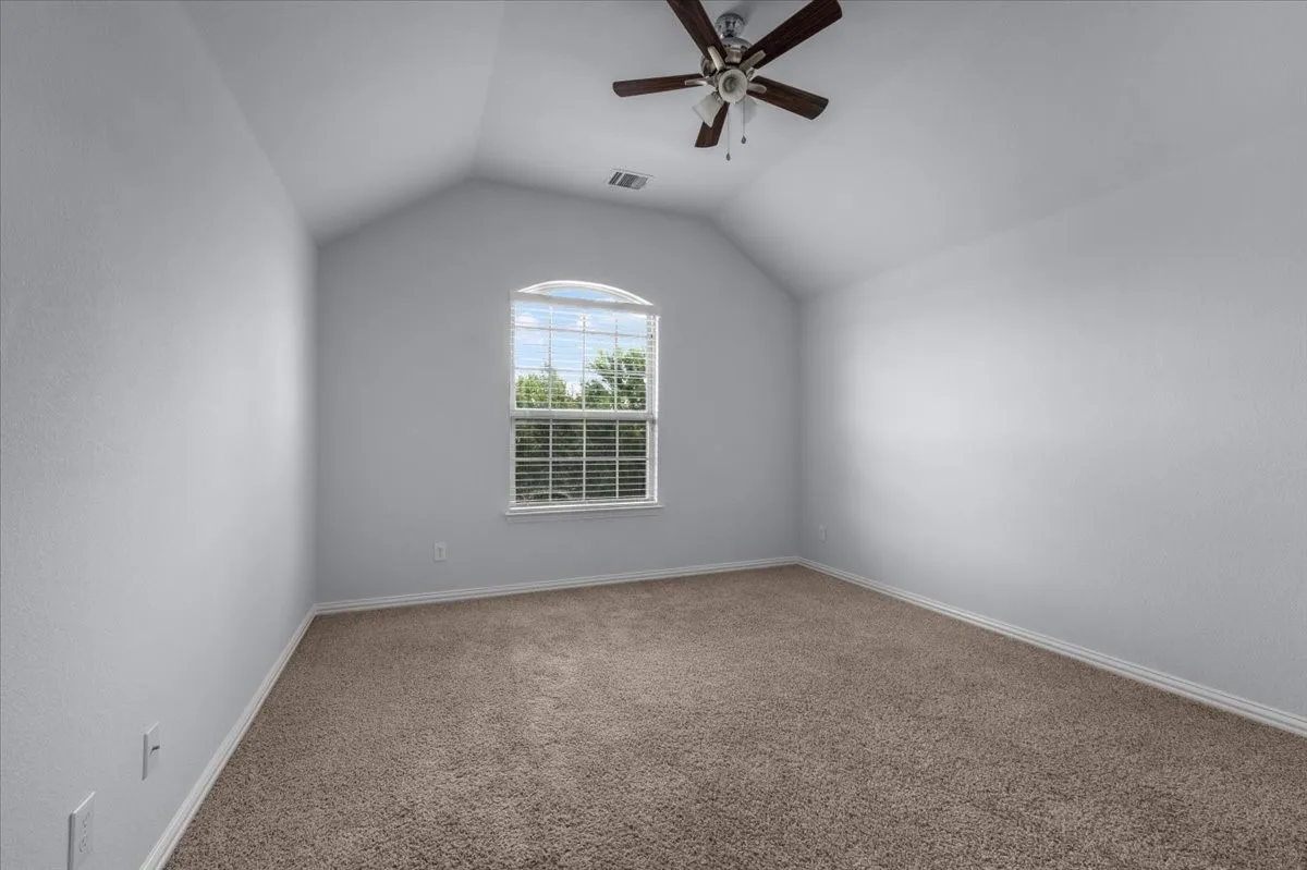 Spacious room featuring vaulted ceilings, a large arched window with blinds, brown carpet flooring, and a ceiling fan with light fixture