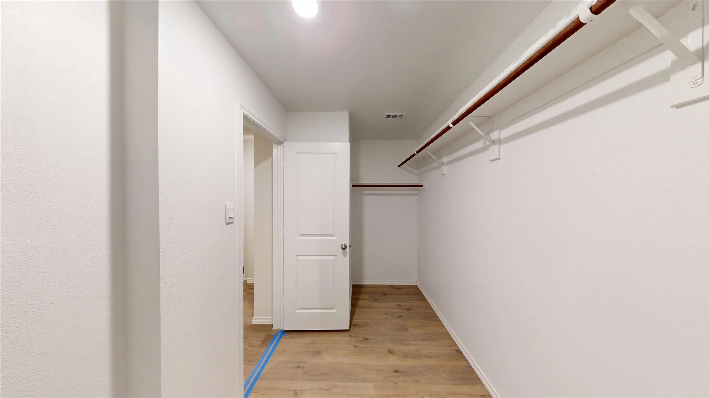 Spacious closet with wood-finish flooring, two-panel interior doors, and built-in shelving with hanging rods