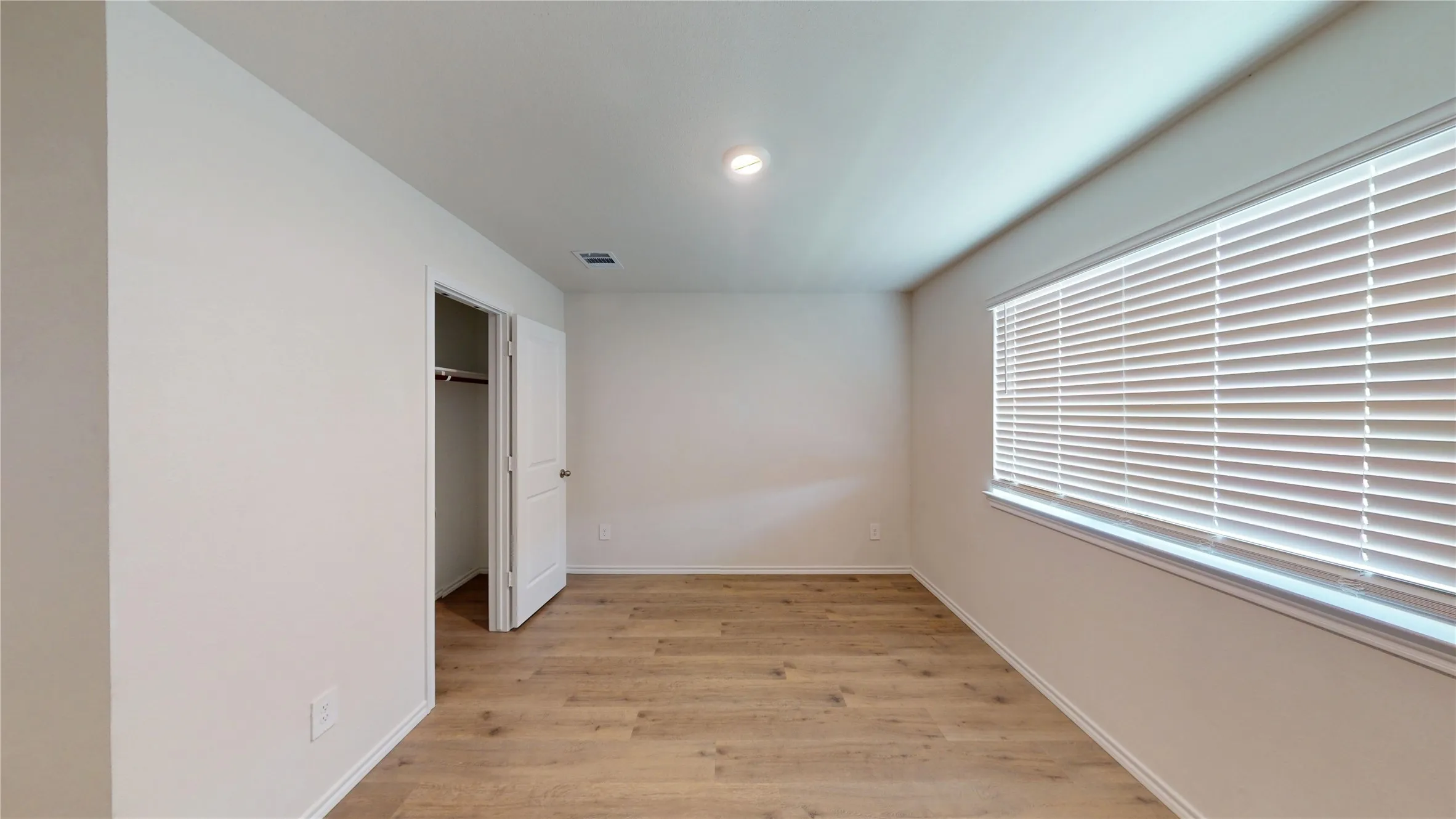 Wood-finish flooring throughout, recessed ceiling lighting, a window with horizontal blinds, and a built-in closet with a swing door