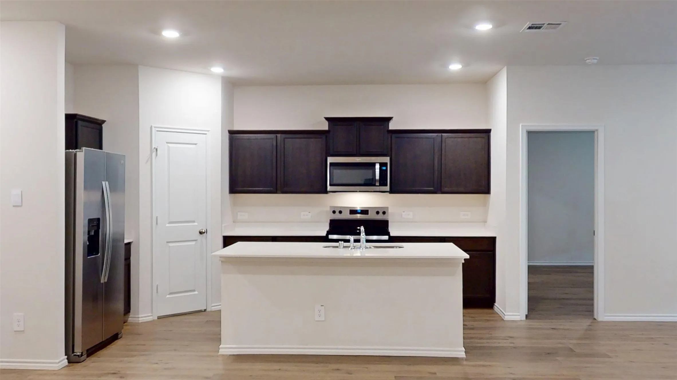 Kitchen featuring dark wood-finish cabinetry, stainless steel appliances, a center island with sink, white countertops, and wood-finish flooring