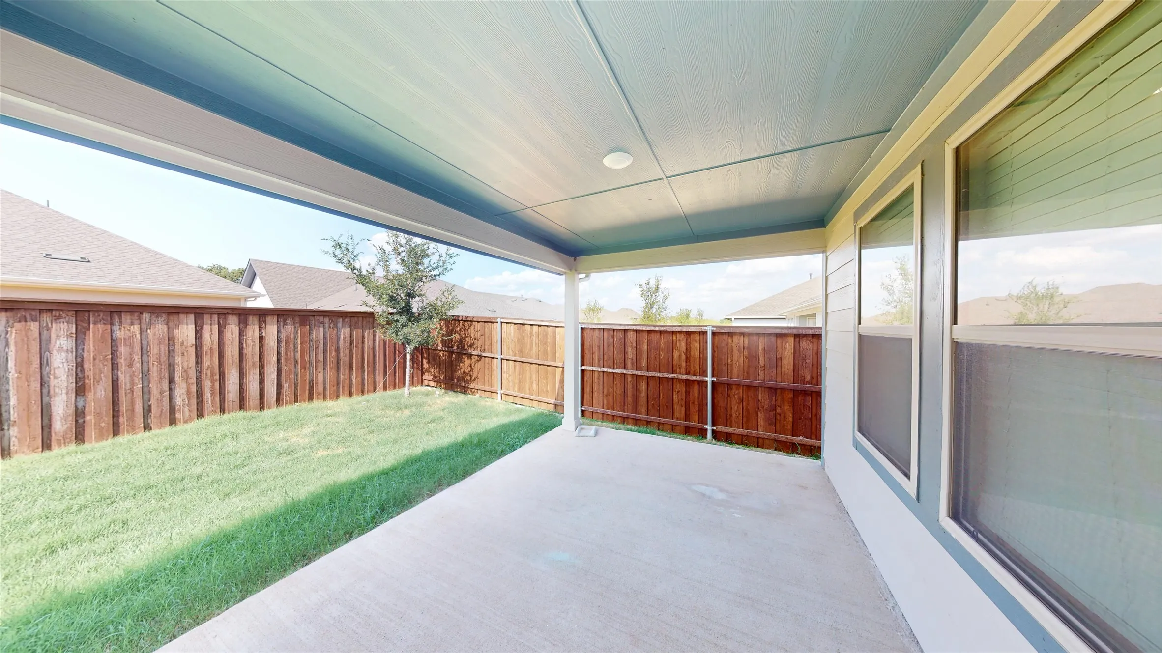 Covered patio with a concrete surface, expansive grassy area, and wood privacy fencing