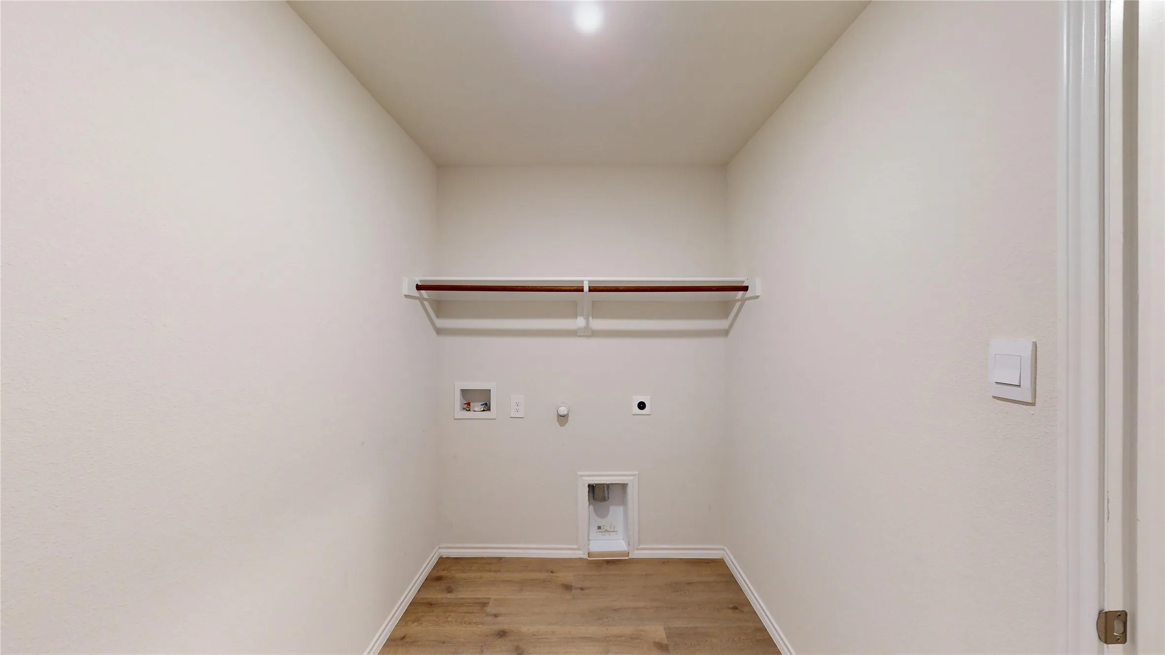 Laundry area featuring wood-finish flooring, light-colored walls, built-in shelving, and a hanging rod