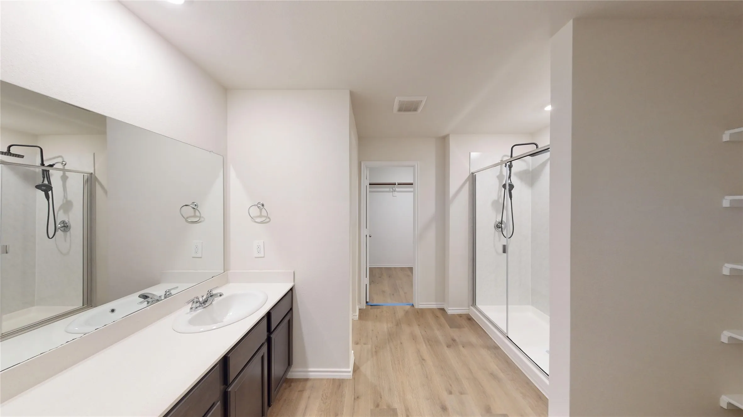 Dual vanity with integrated sink, wood-finish flooring, glass-enclosed shower, and built-in shelving