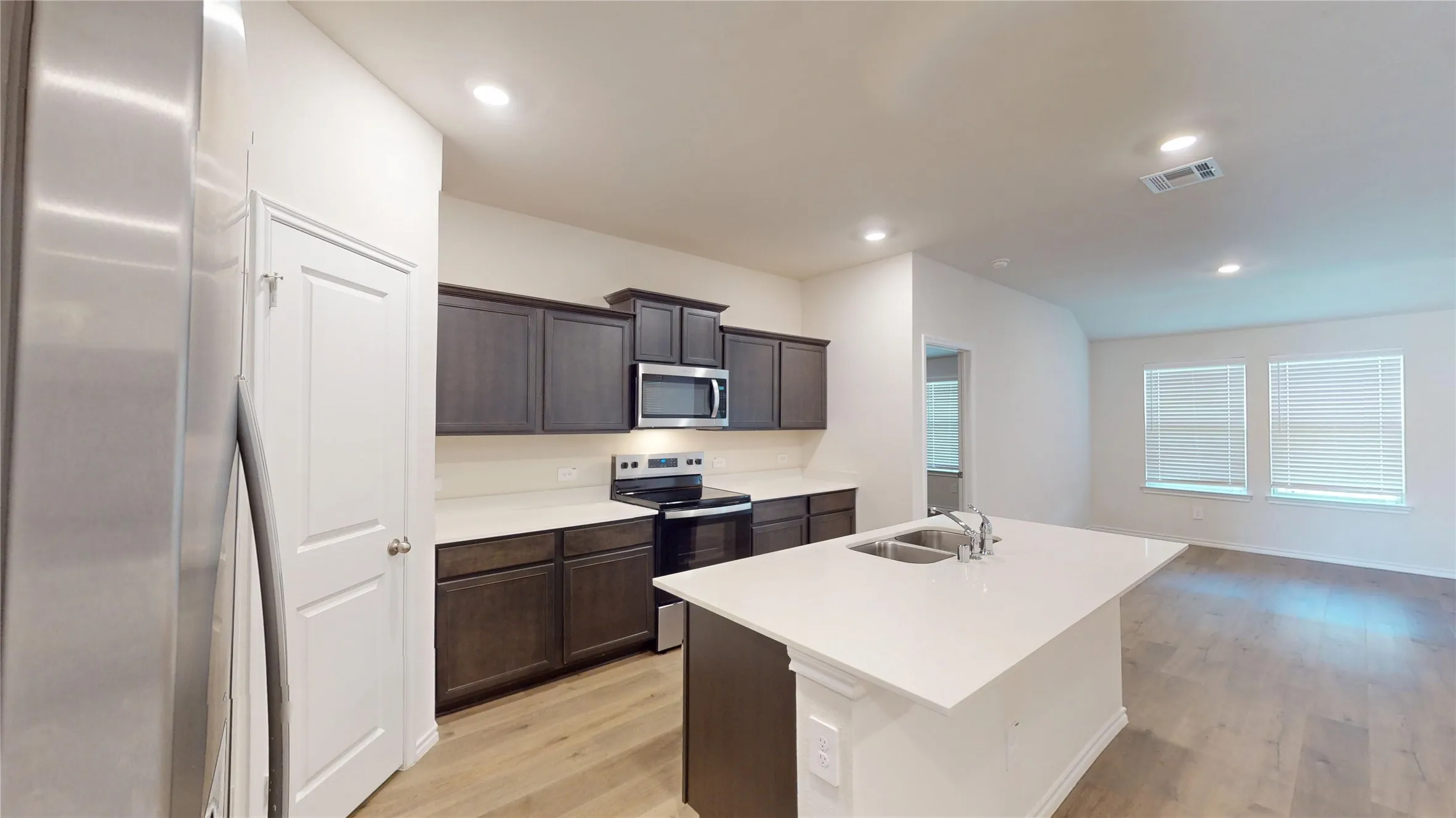 Kitchen featuring wood-finish flooring, dark wood cabinetry, white countertops, stainless steel appliances, and a kitchen island with an integrated sink